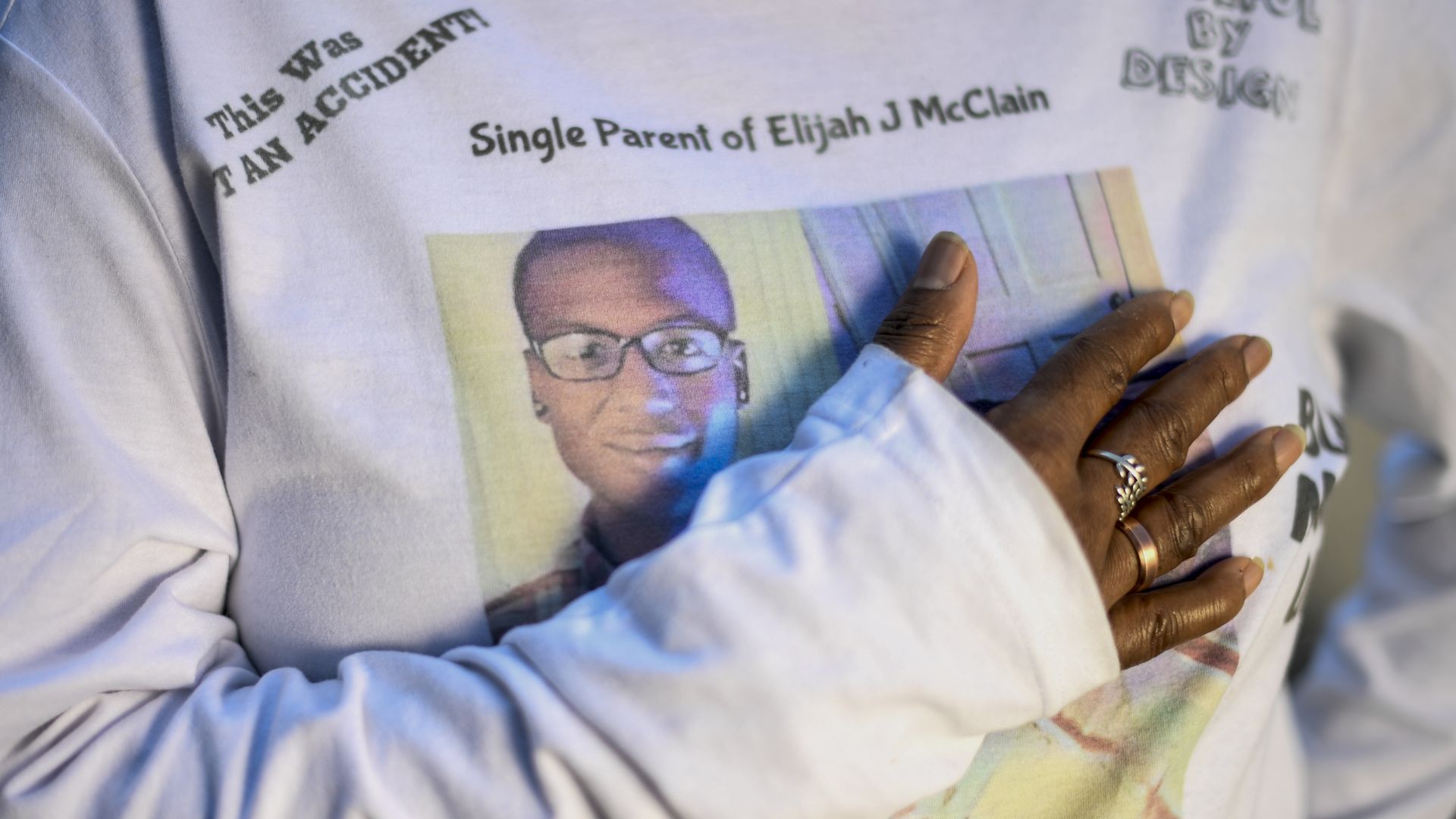 Photo of a person's hand held to her chest as she wears a T-shirt with Elijah McClain's picture on it