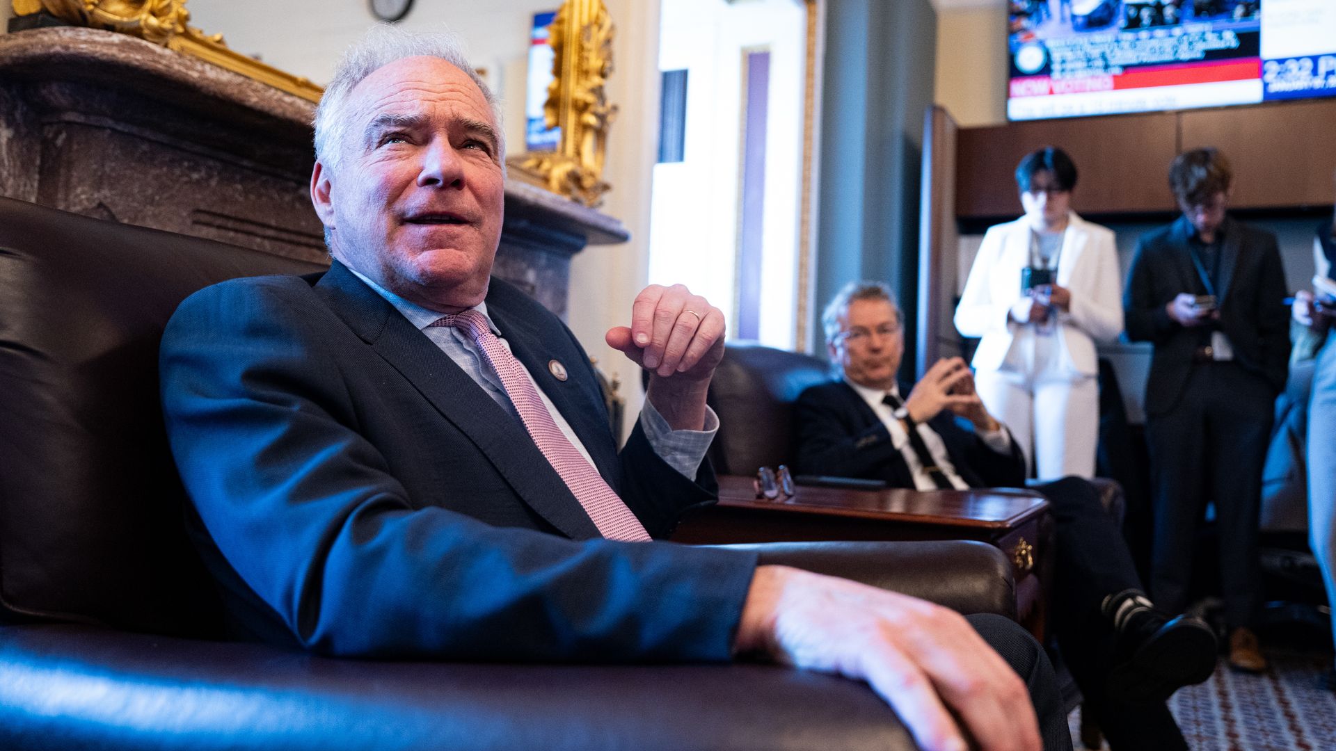 Senators Tim Kaine and Rand Paul standing at a briefing podium with microphones and reporters’ notepads visible.