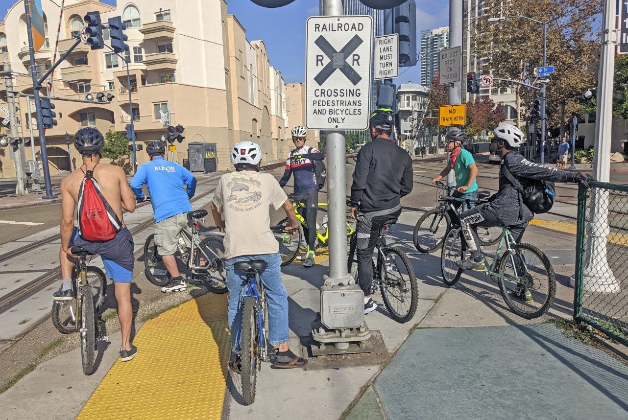 A group of seven cyclists wait at an intersection downtown. 