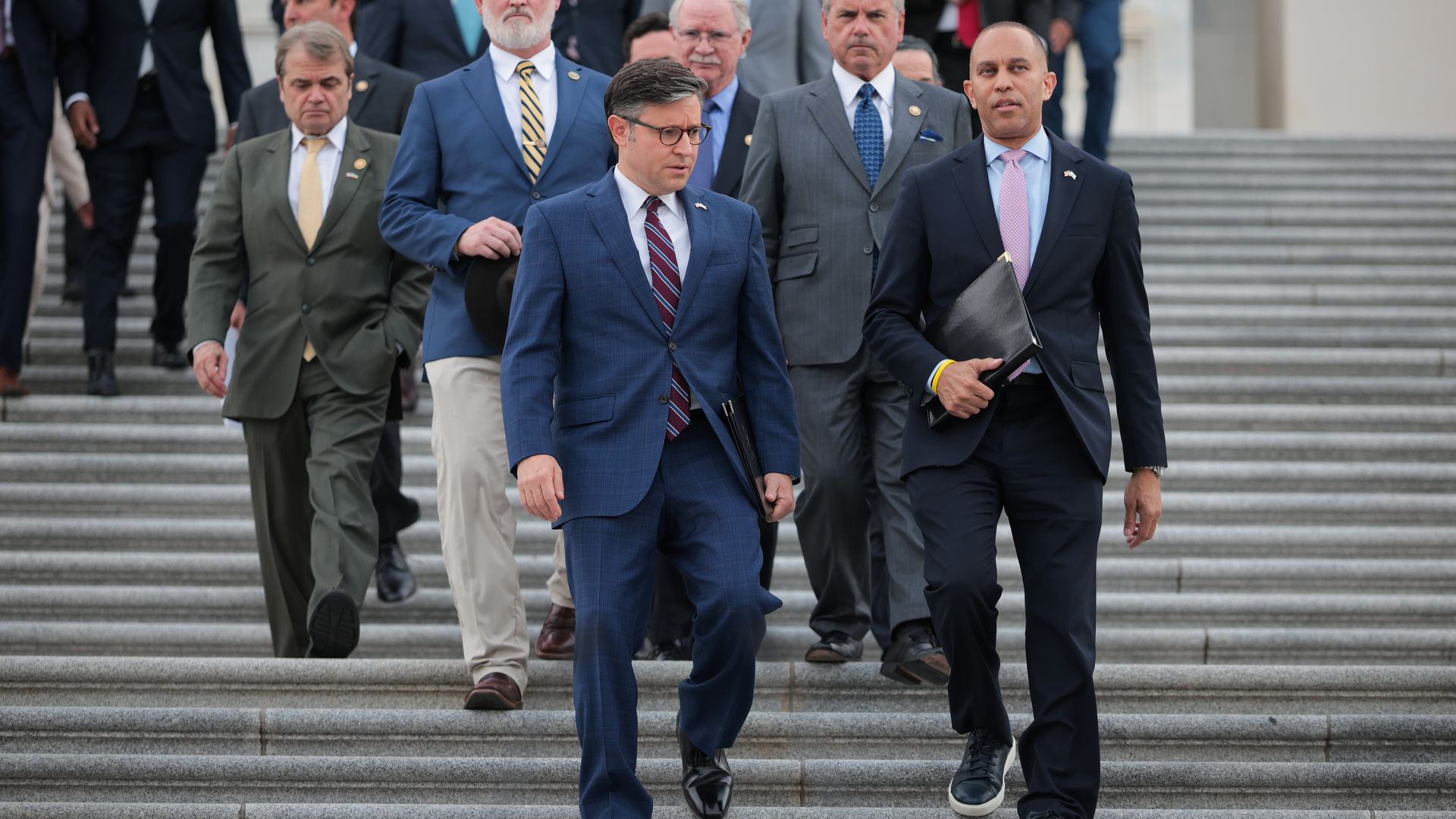 Mike Johnson and Hakeem Jeffries, both wearing blue suits, walk down the U.S. Capitol steps in front of a group of House members.