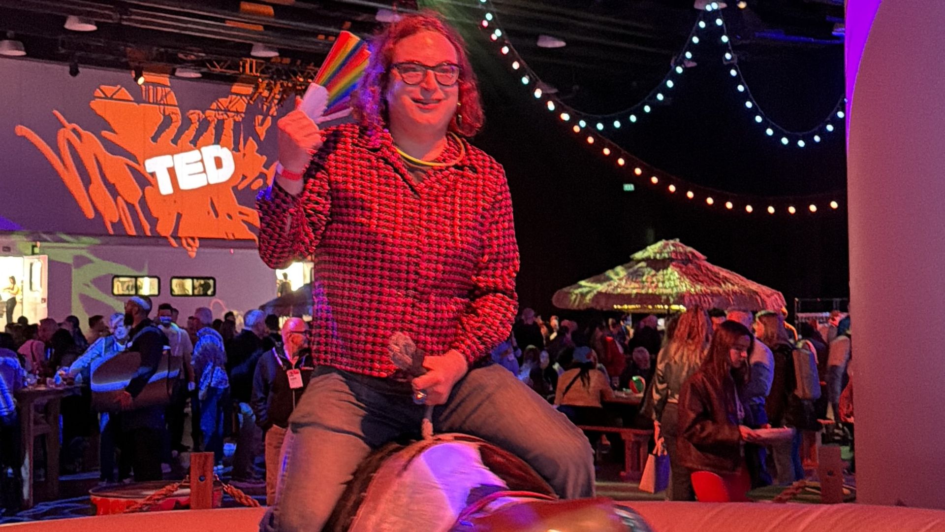 Ina Fried rides a large inflatable horse on a circular red arena at a TED event, with colorful lights and a crowd in the background.