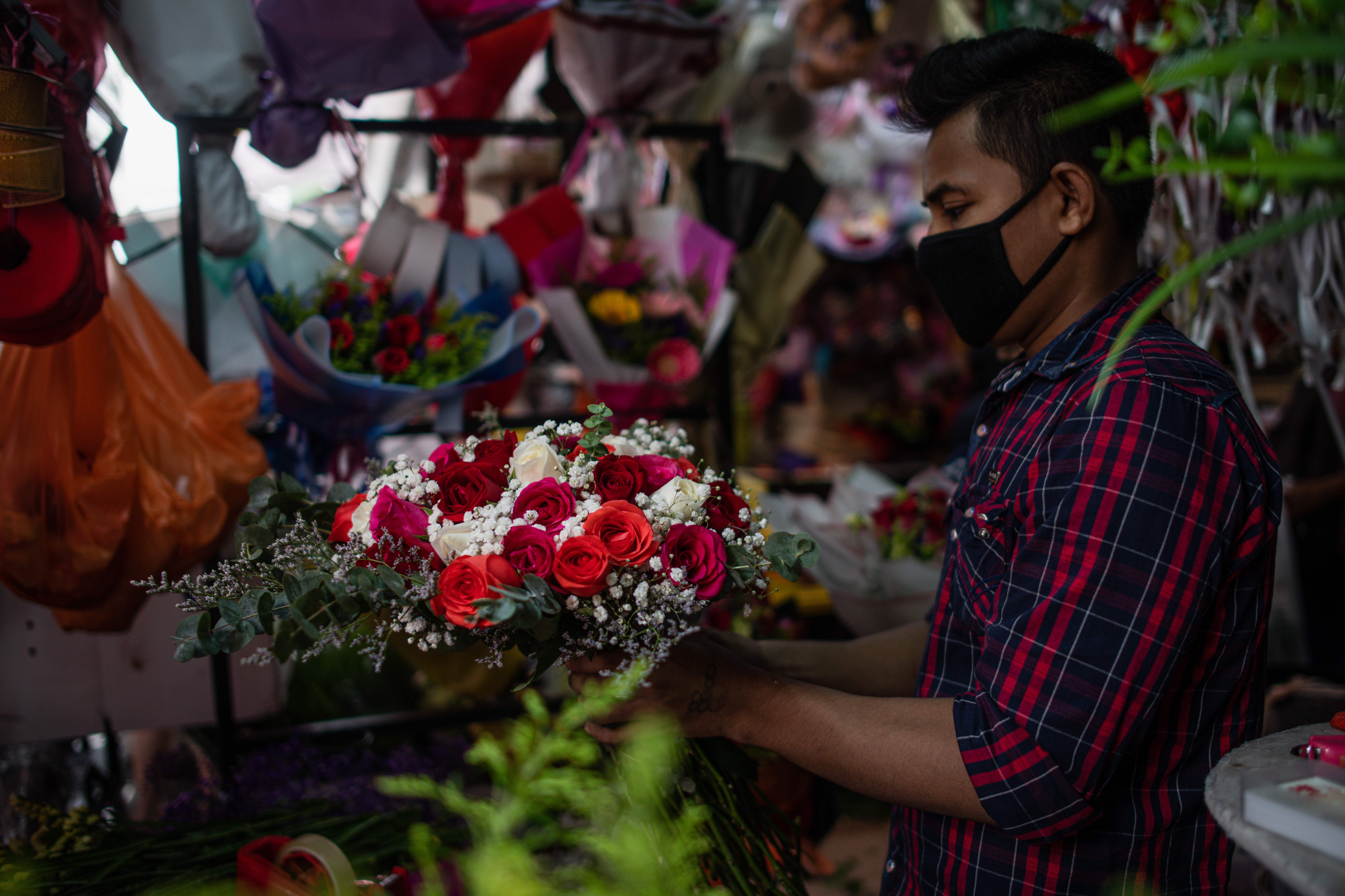 In this image, a man wears a face mask and adjusts flowers