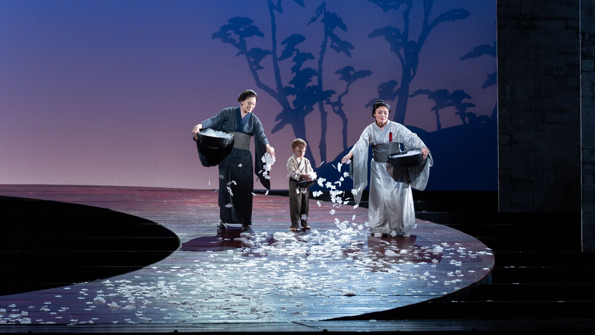 Photo of 2 women and a boy on stage, spreading flowers down a path. 