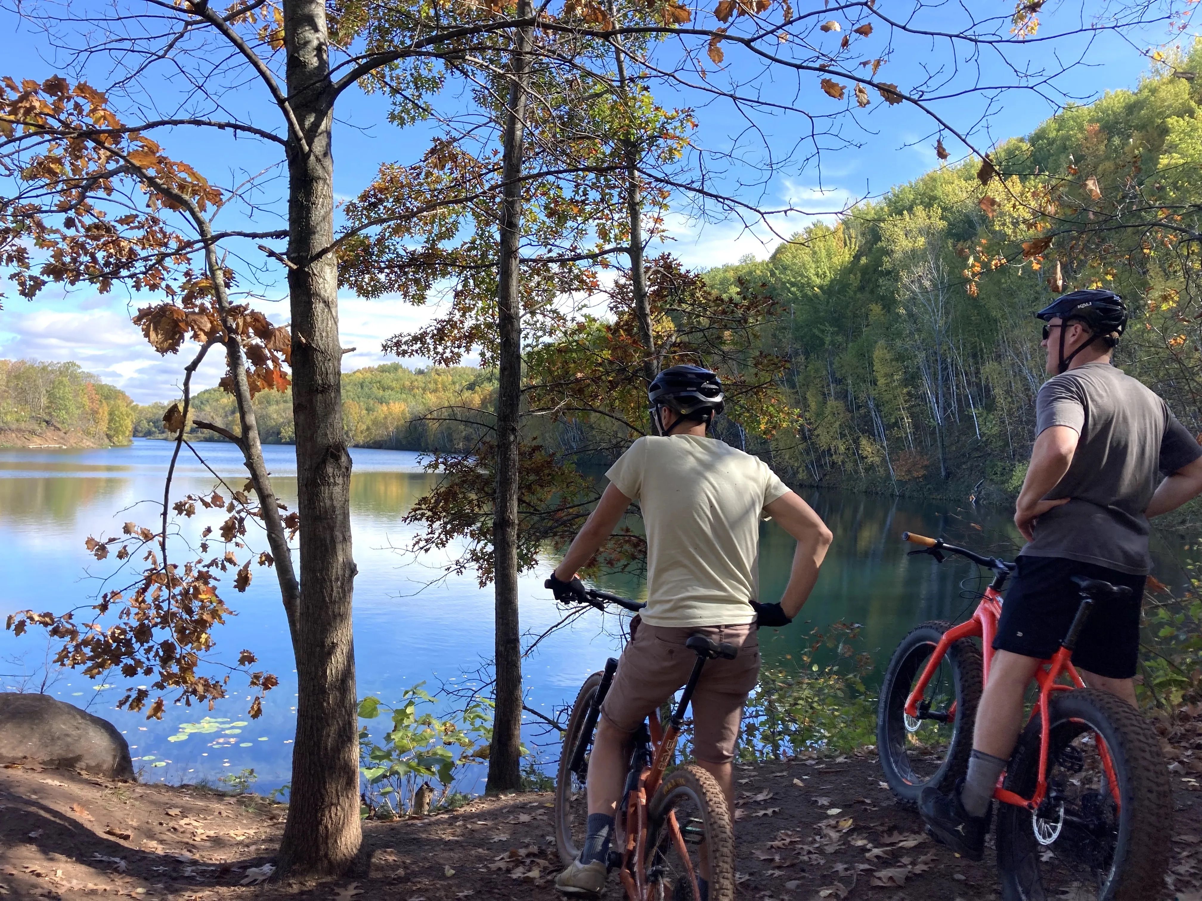 Two people on bikes in front of a lake.