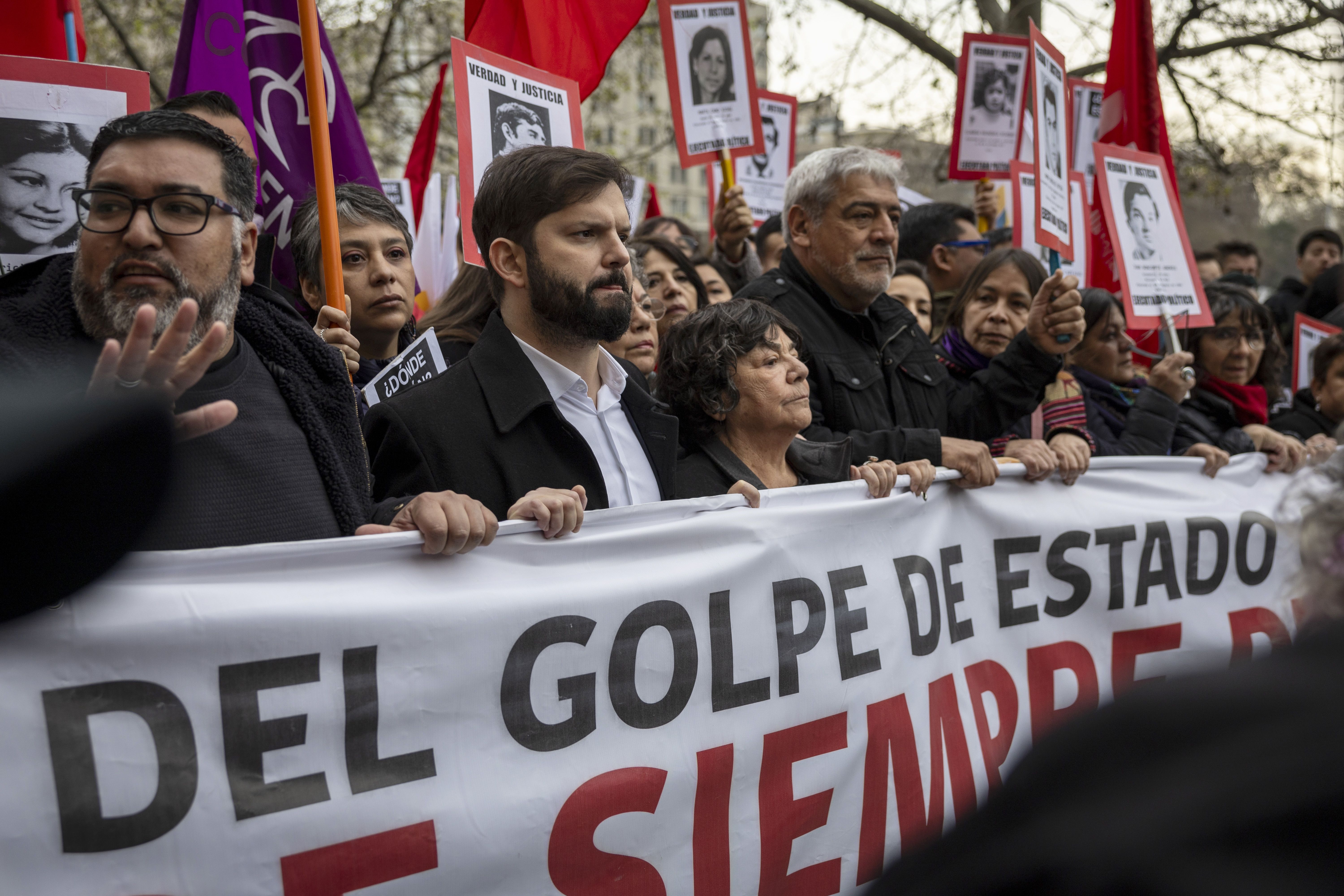 Chilean President Gabriel Boric and several others march on the 50-year mark of the coup that led to the dictatorship of Augustin Pinochet. They are holding a large white banner. 