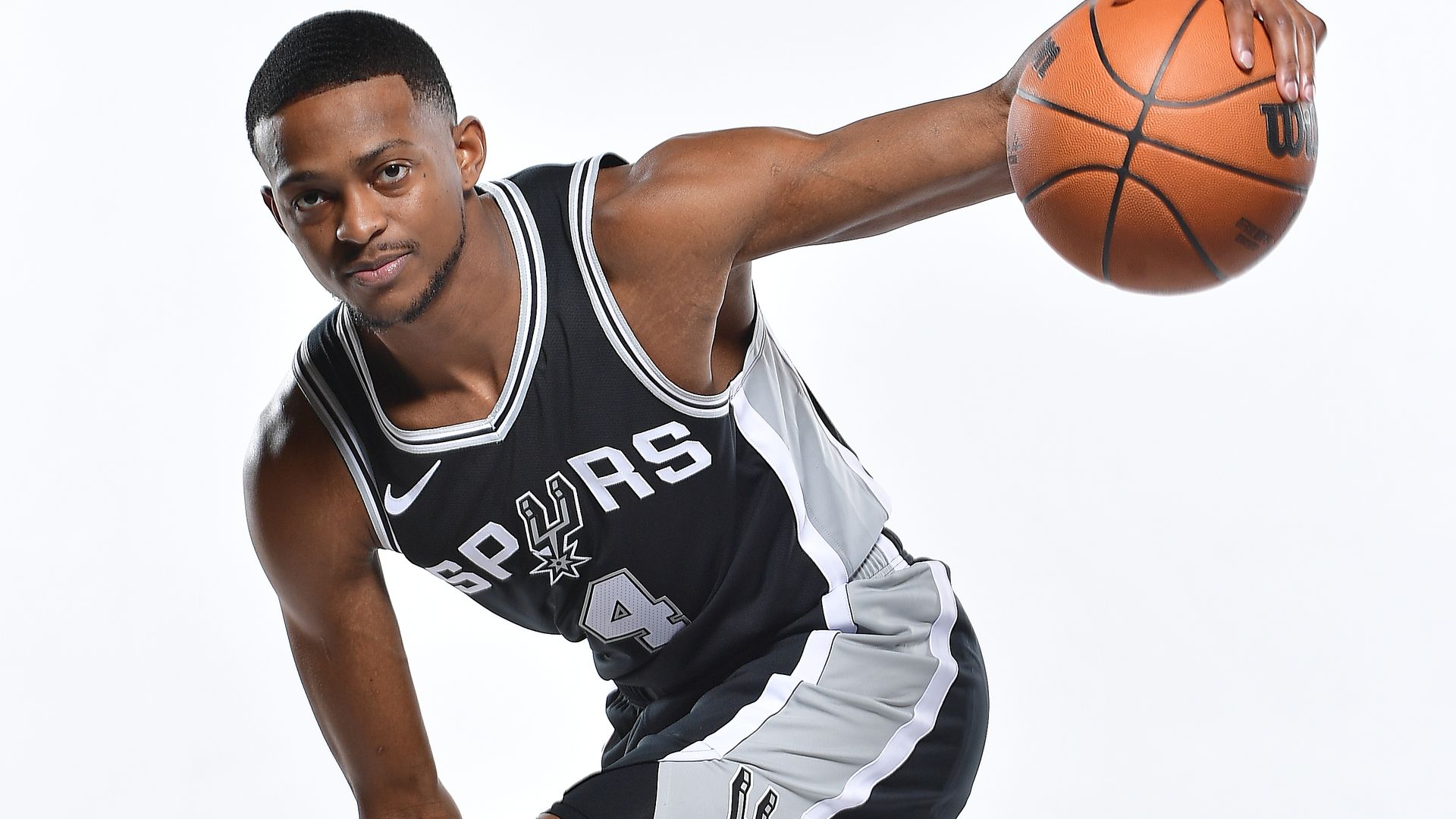 De'Aaron Fox palms a basketball while wearing a Spurs jersey.
