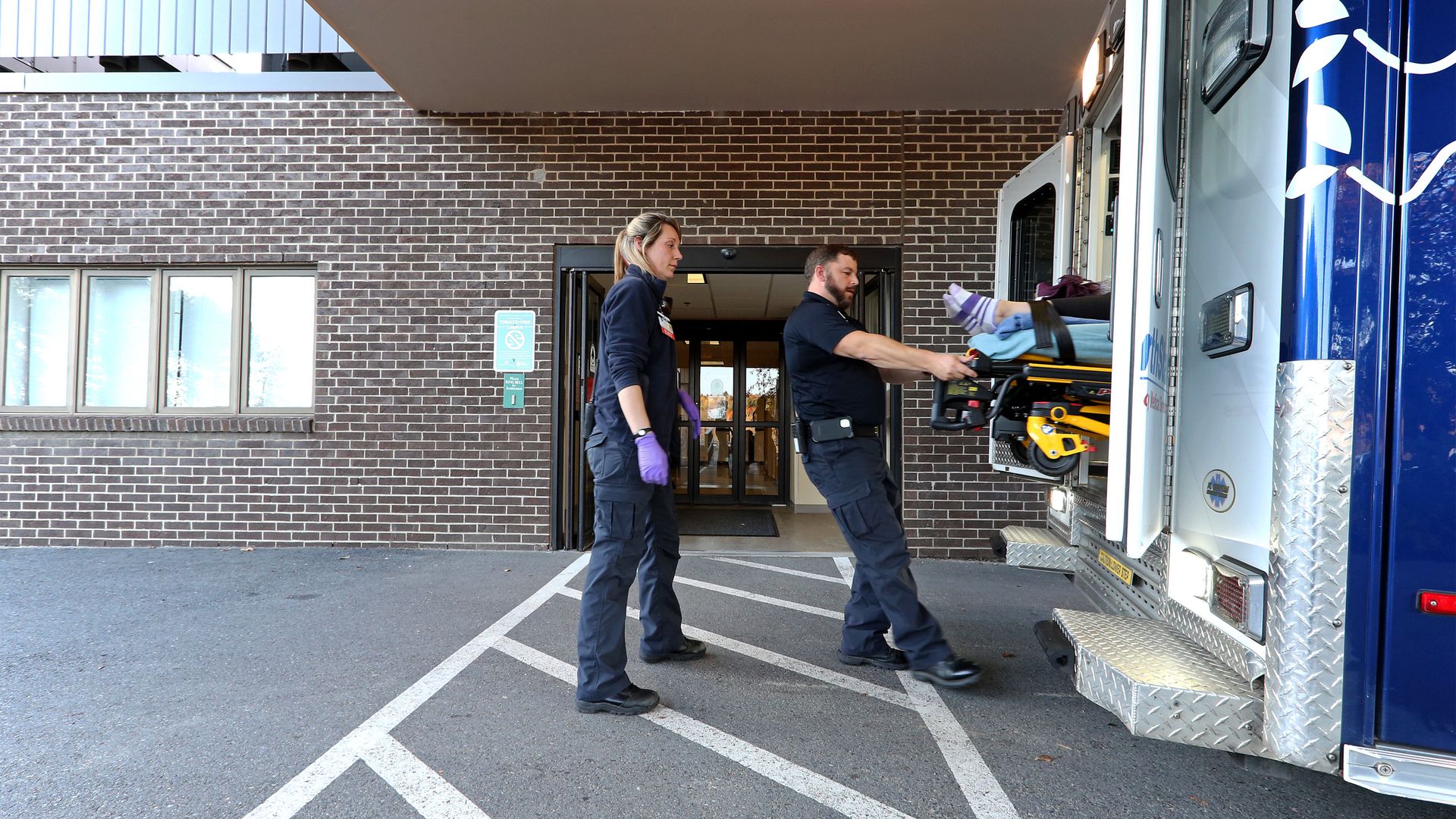 Two EMTs pull a patient out of an ambulance outside of a hospital.
