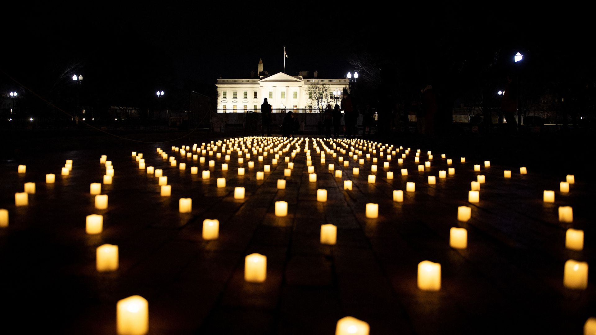People walk past electric candles from a vigil in Lafayette Park for nurses who died during the COVID-19 pandemic on January 13, 2022, in Washington, DC.