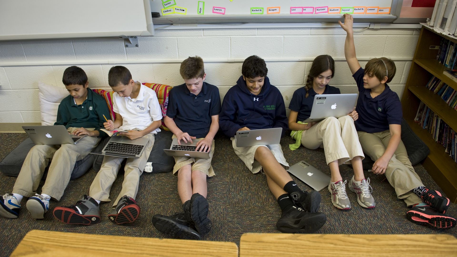 Sixth grade students sit against a wall and work on laptops
