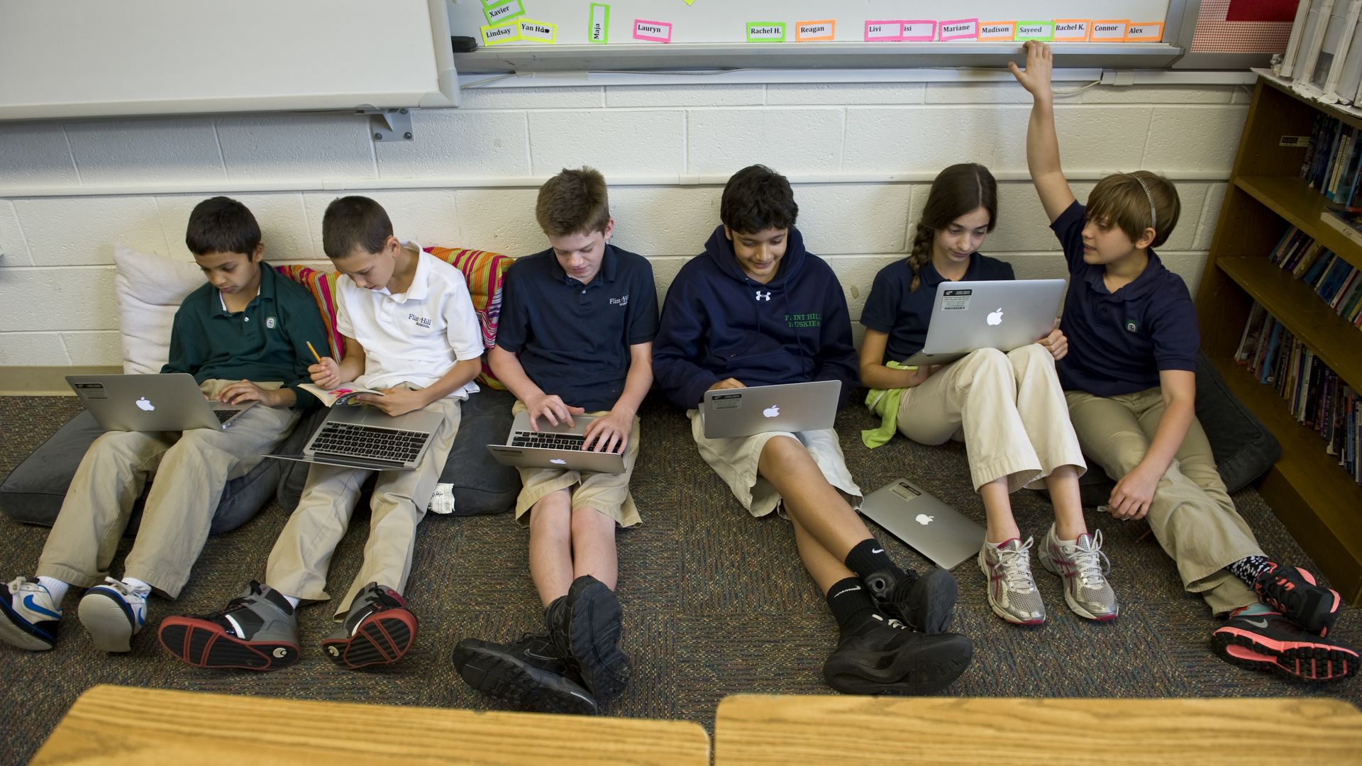 Sixth grade students sit against a wall and work on laptops