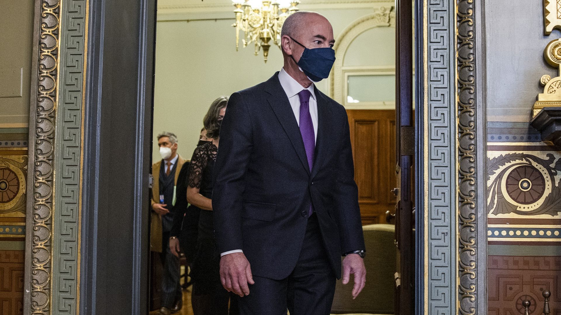 DHS Secretary Alejandro Mayorkas wearing a mask and walking through a doorway