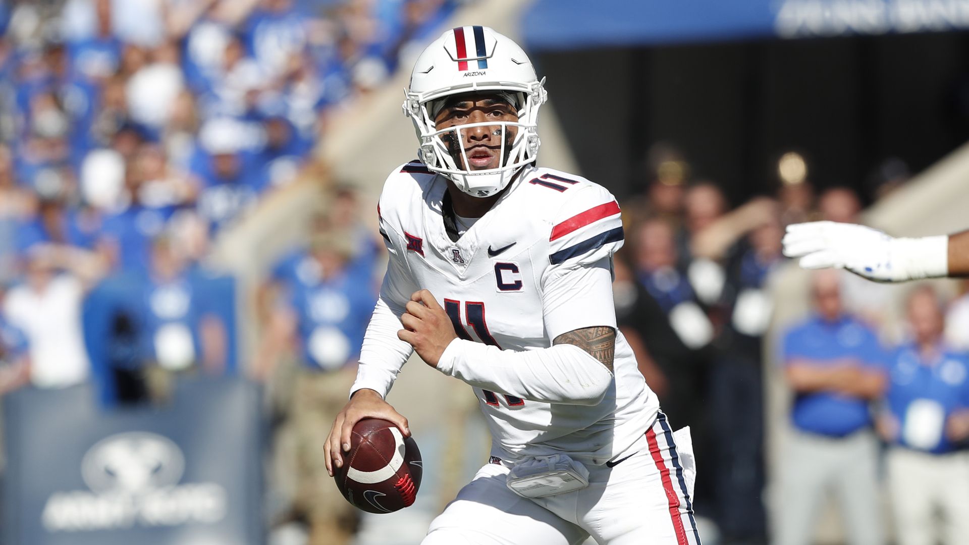 Arizona quarterback Noah Fifita holding ball, preparing to throw during a game with crowd in blue in the background.