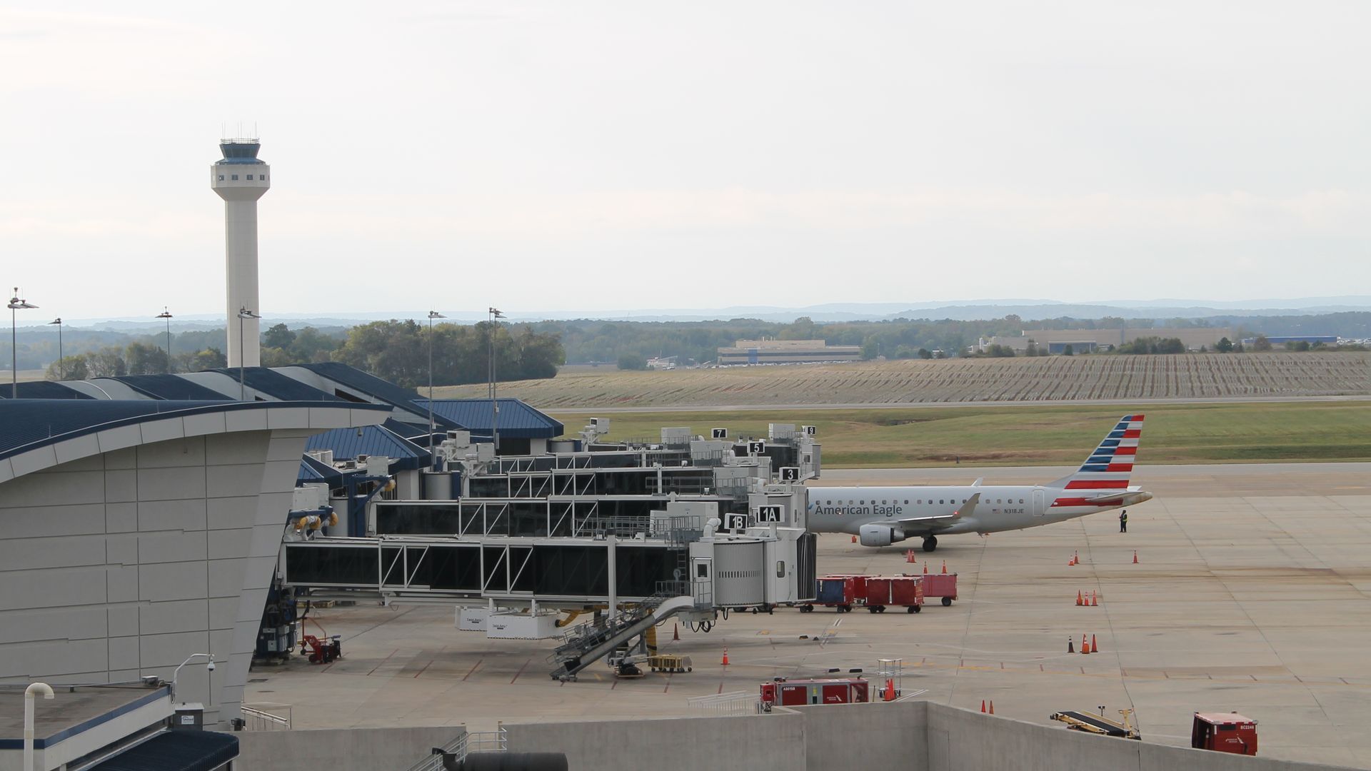 Airport terminal with jet bridges and an American Eagle plane parked on the tarmac near a control tower under a cloudy sky.