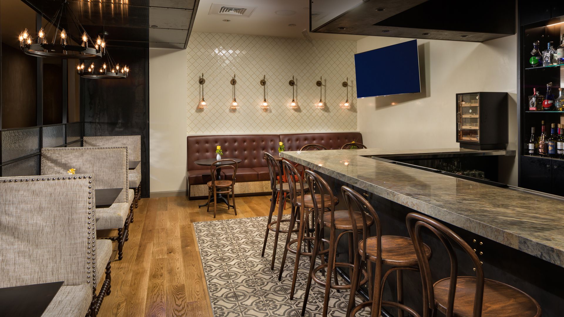 A chic bar at Dorrego's features a marble counter with brown wood stools, banquettes in the back, gray patterned tile floor alongside wood, small tables with yellow flowers, pendant lights, and bottle shelves at the bar.