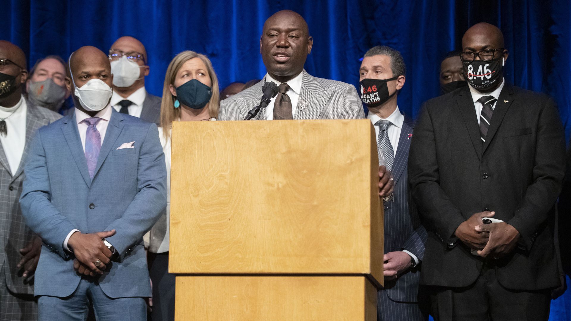 A group of people wearing suits and face masks stands behind a podium