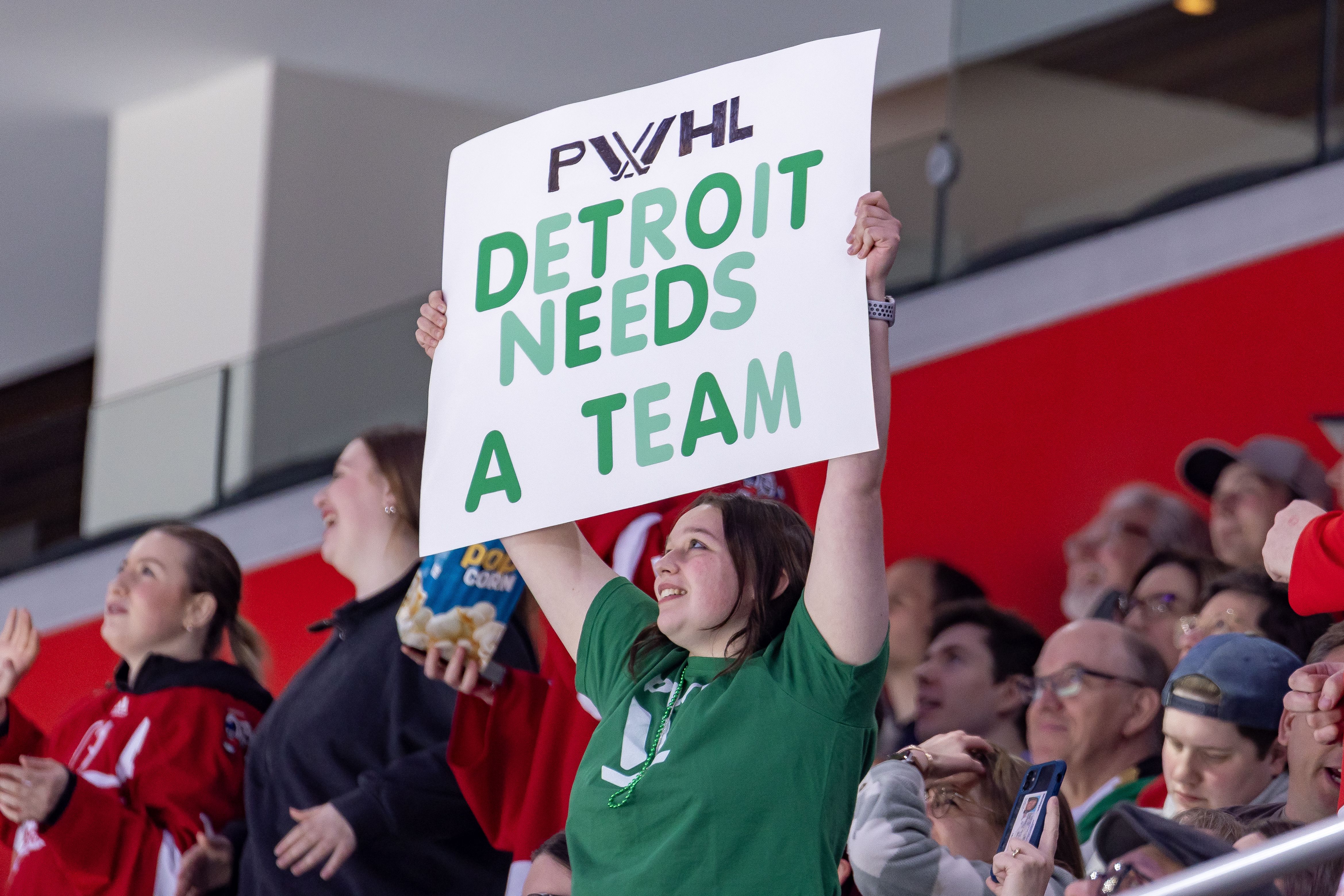 A fan holds up a sign that says PWHL Detroit needs a team 