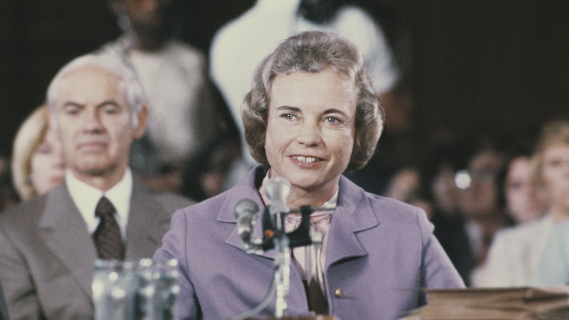 Sandra Day O'Connor smiles while seated in front of a microphone microphones during her Senate confirmation hearing. 