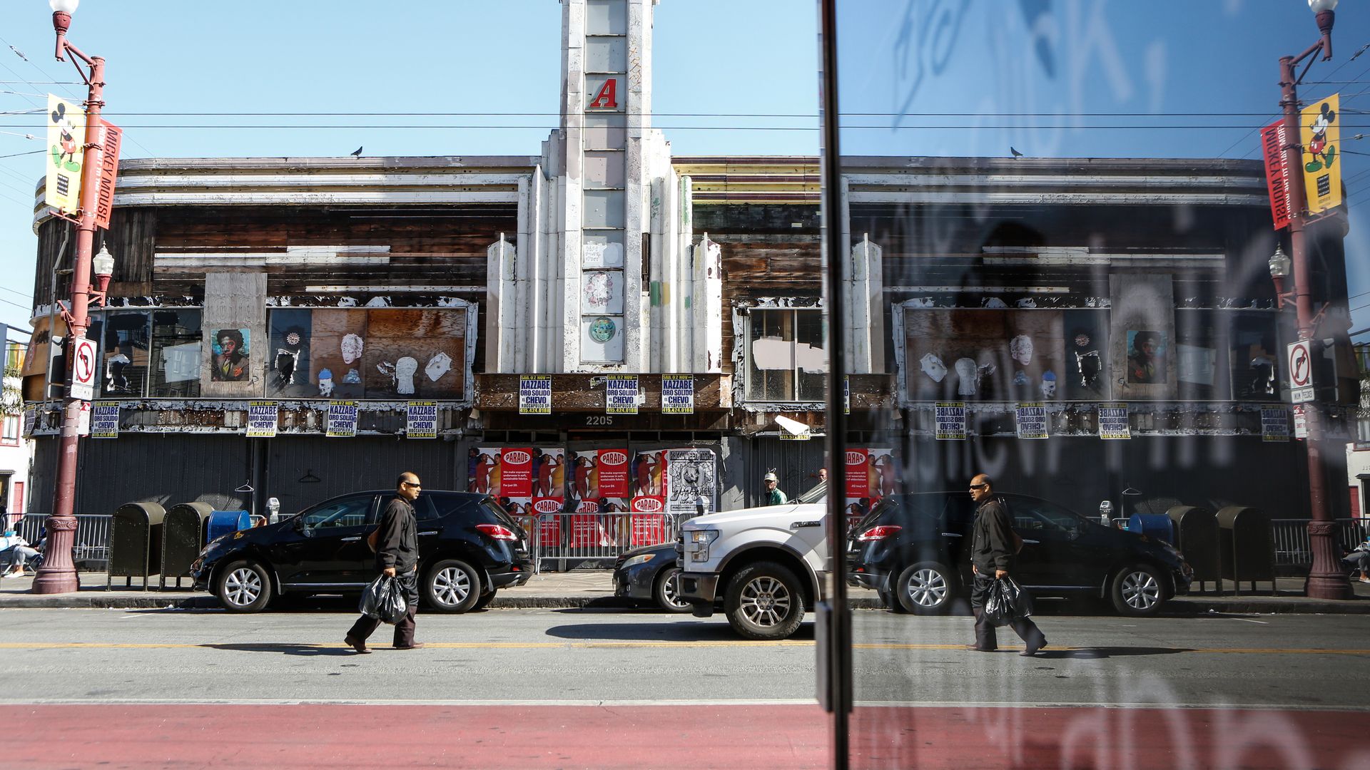 Photo of a person walking down a street next to a boarded-up vacant building
