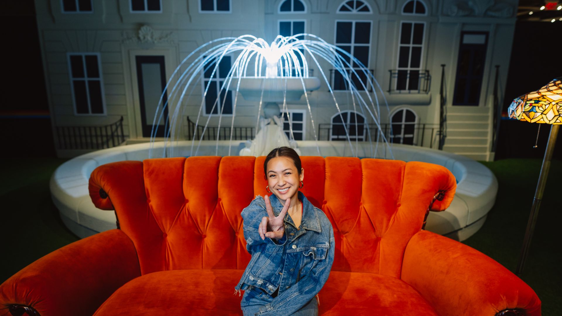 A woman poses on a couch in front of a fake fountain at "The Friends Experience"