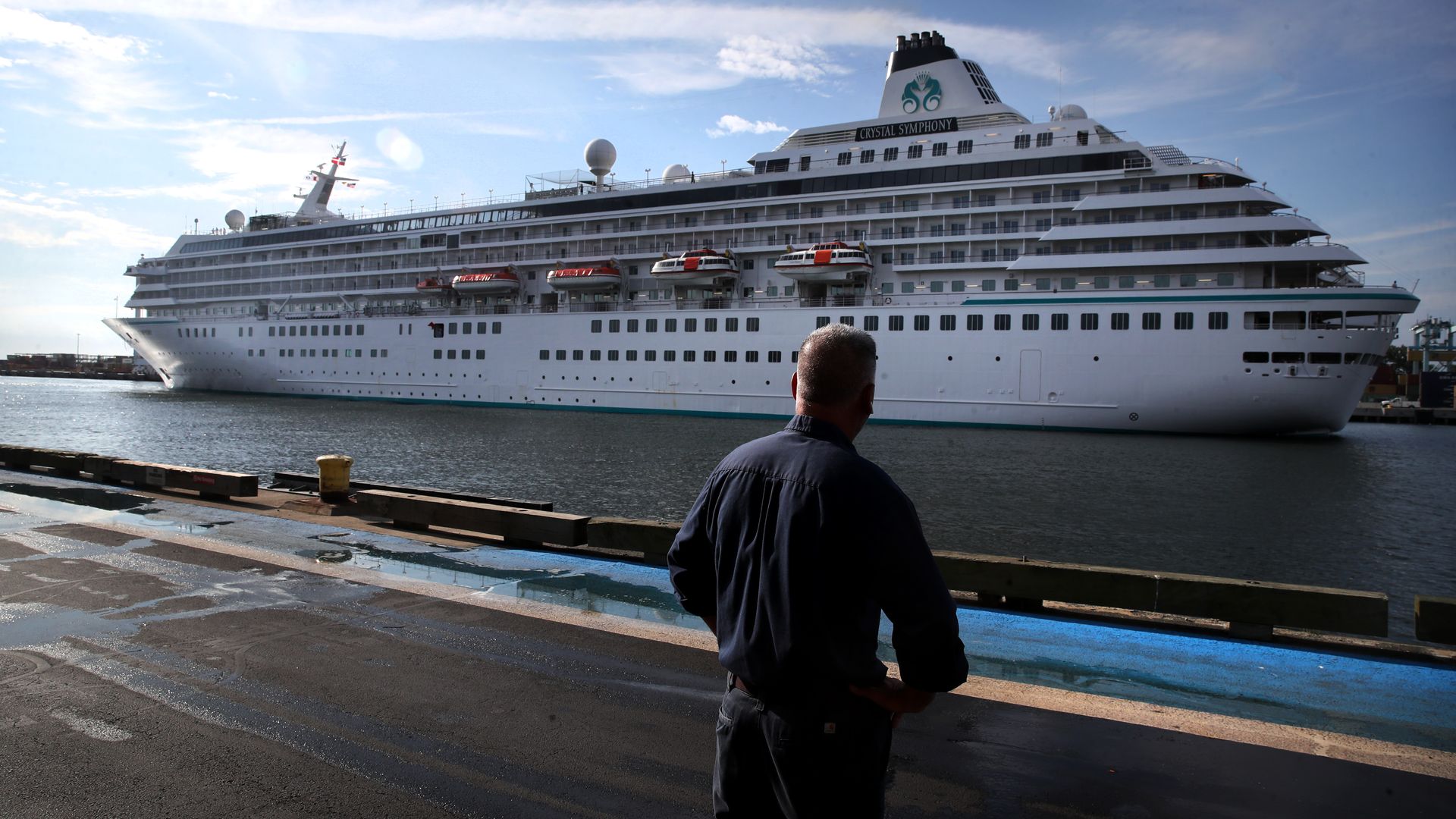 A man stands on a dock watching a cruise ship in the water