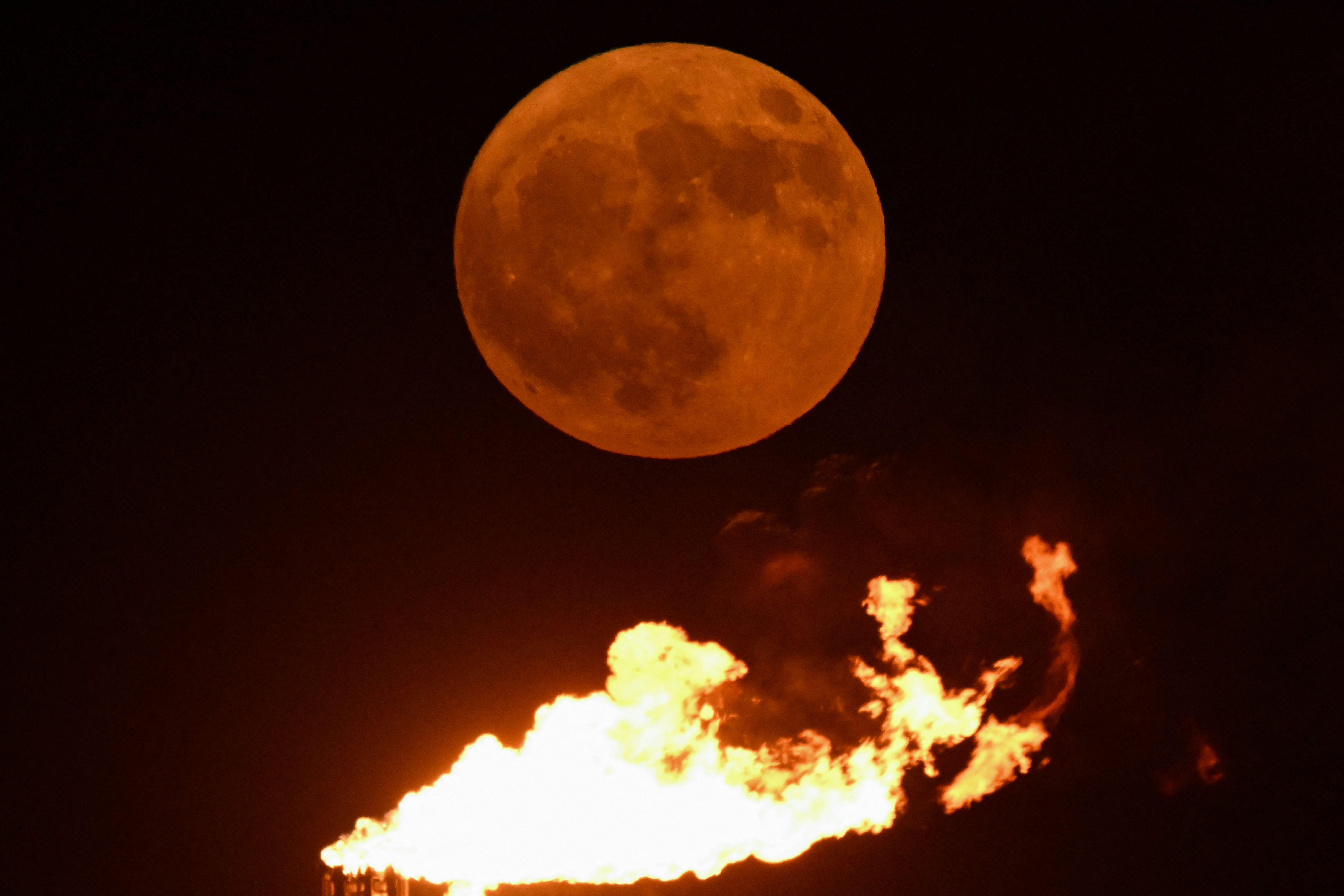 A Super blue moon rises over the flare stacks of an oil field near the southern port city of Basra on August 19, 2024. 