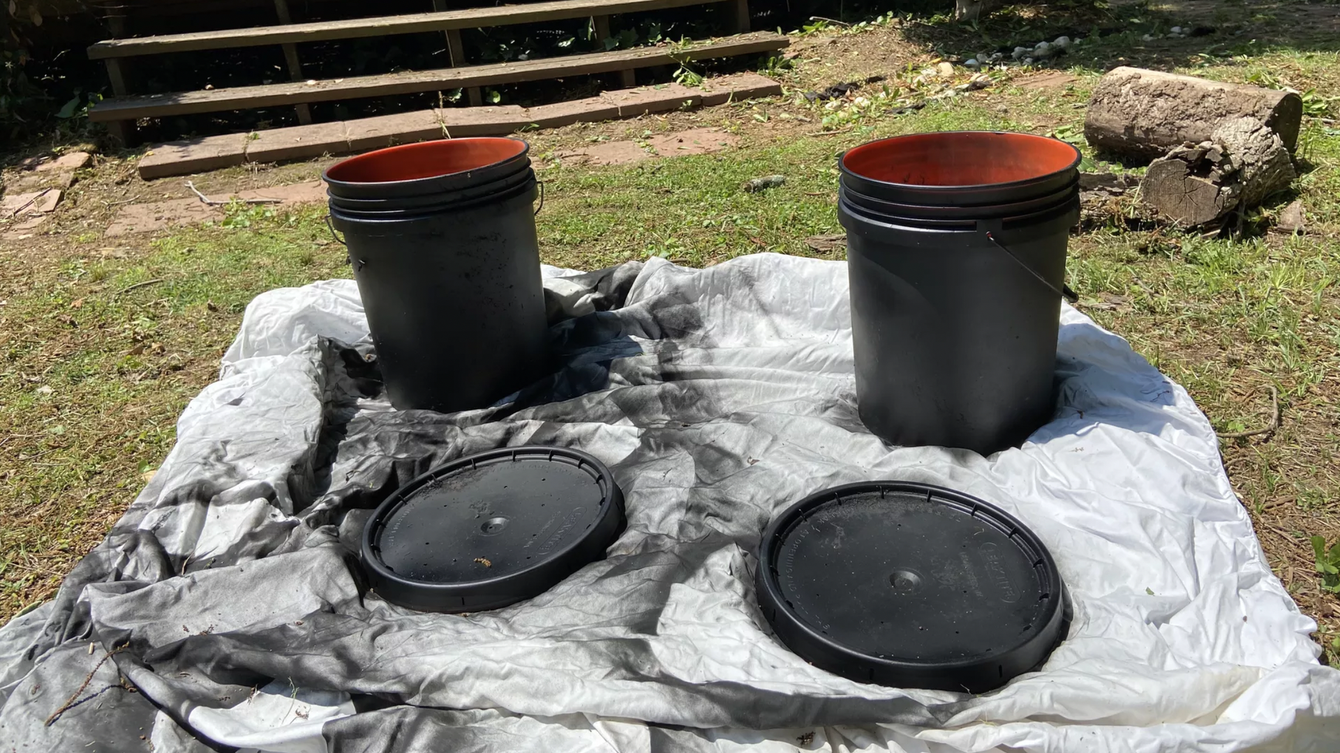 Two black spray-painted buckets that will be used as mosquito traps on a white sheet 