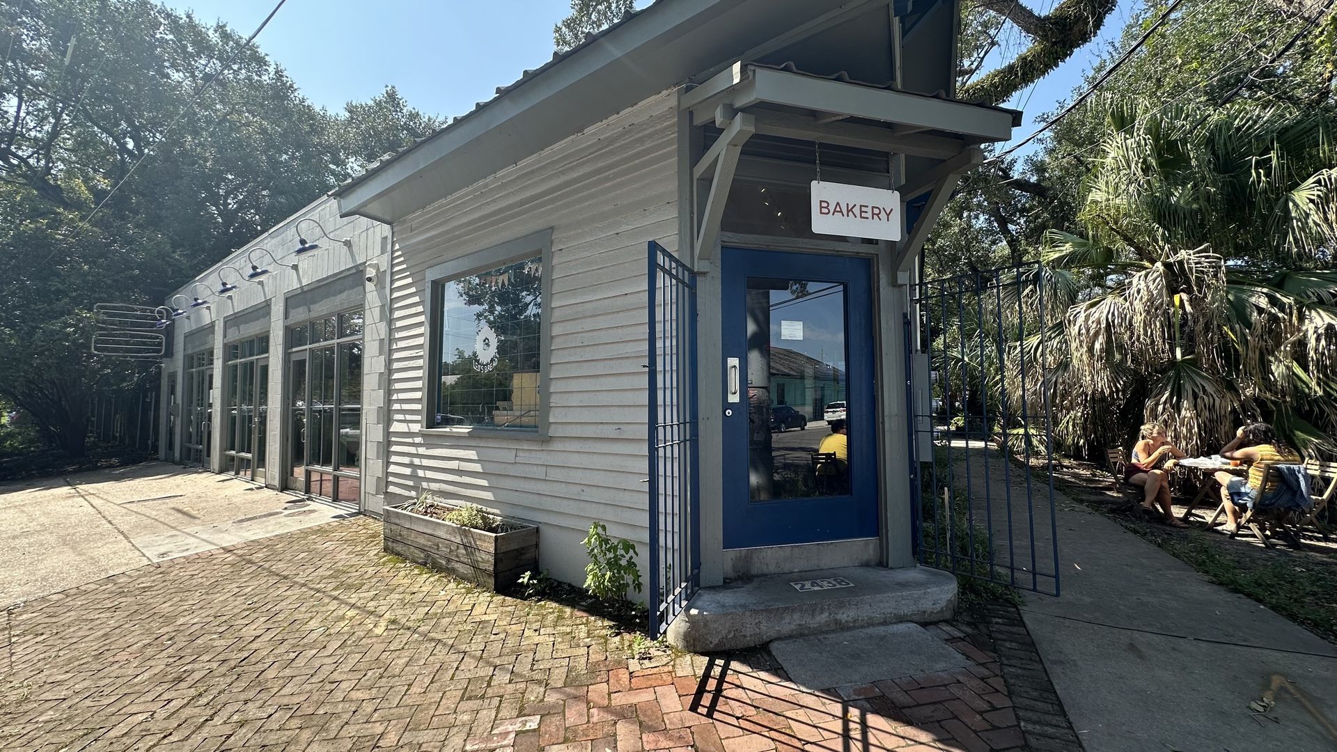 A corner building has a blue door and a sign that says "bakery" hanging over it.