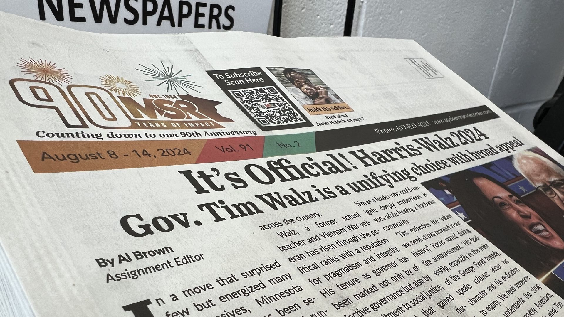 The front page of a Minnesota Spokesman-Recorder newspaper on a newstand with a banner headline declaring: "It's Official! Harris-Walz 2024." The newspaper's "MSR" logo with a "90" and fireworks icons are in the top left corner of the page.