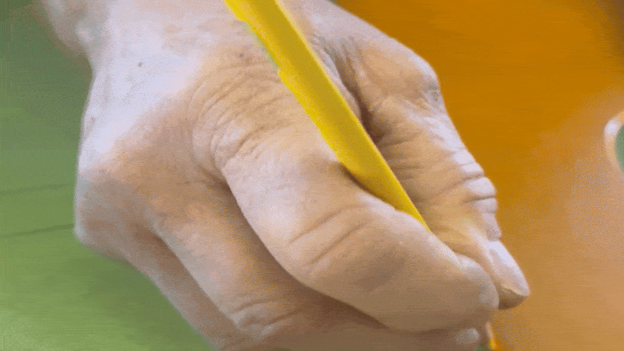 Close-up of a hand holding a yellow pencil, writing on a green and orange surface.