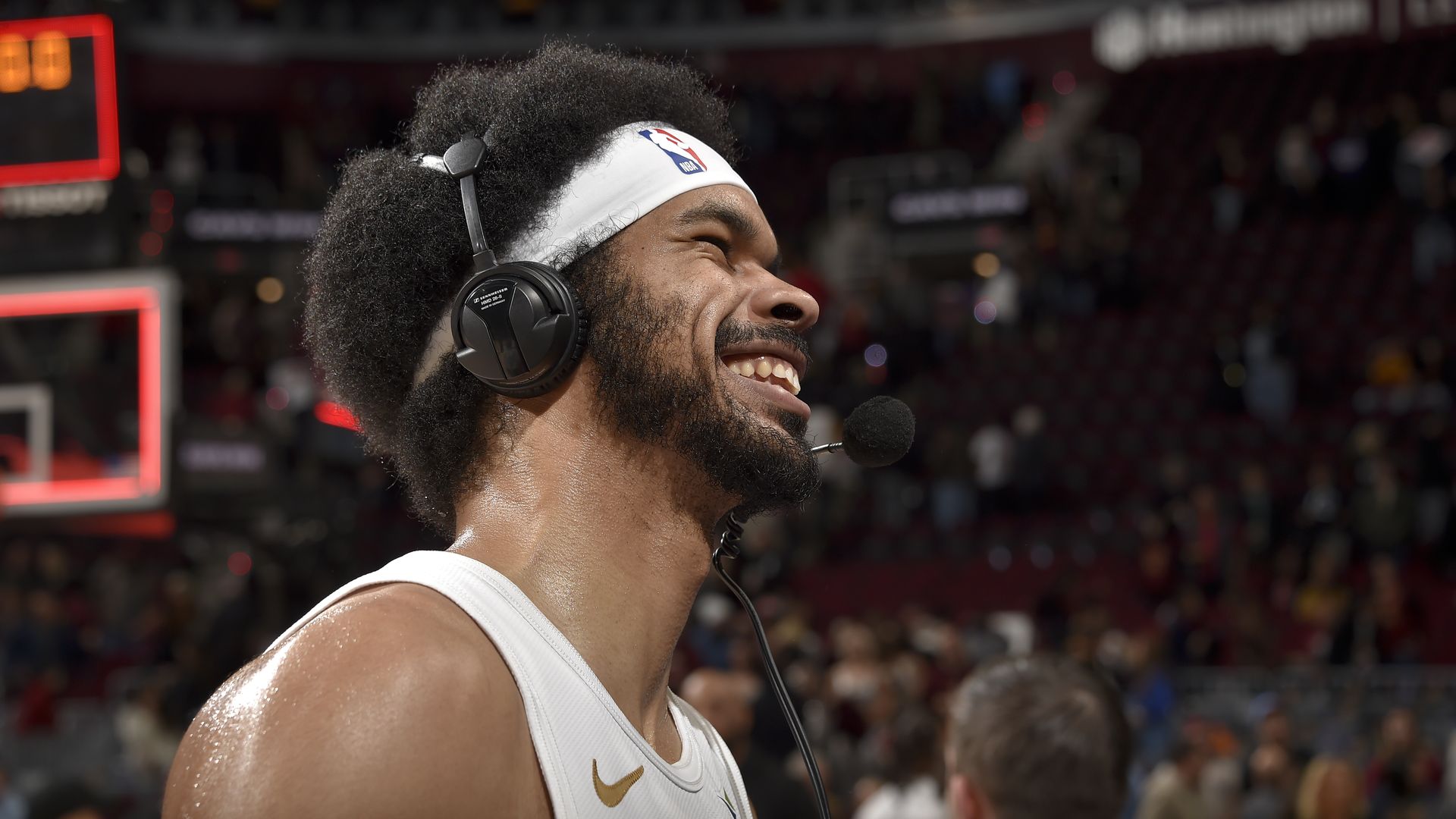 Man with afro smiles while talking into headset on basketball court