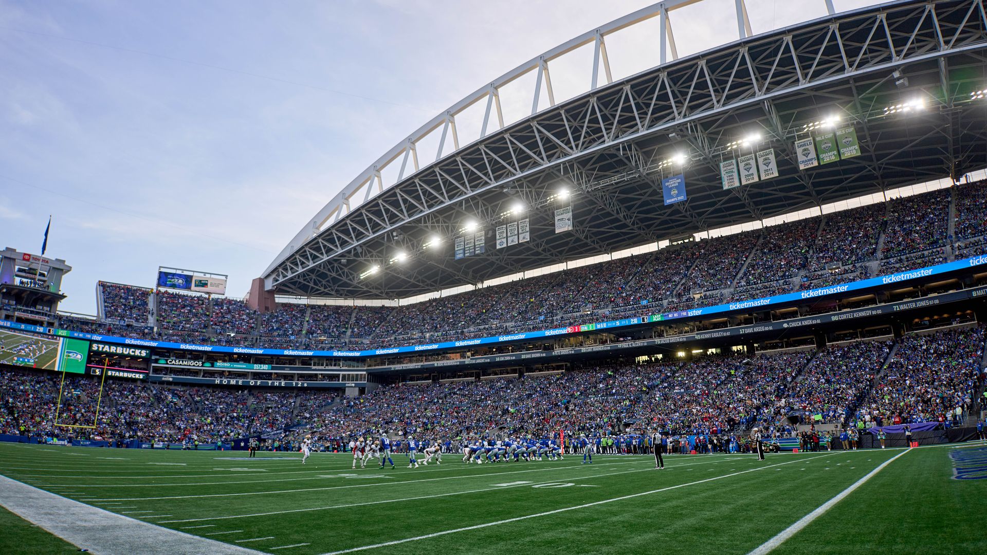 Light dwindles behind Lumen Field as it is filled with fans; the artificial turf field is in the foreground.