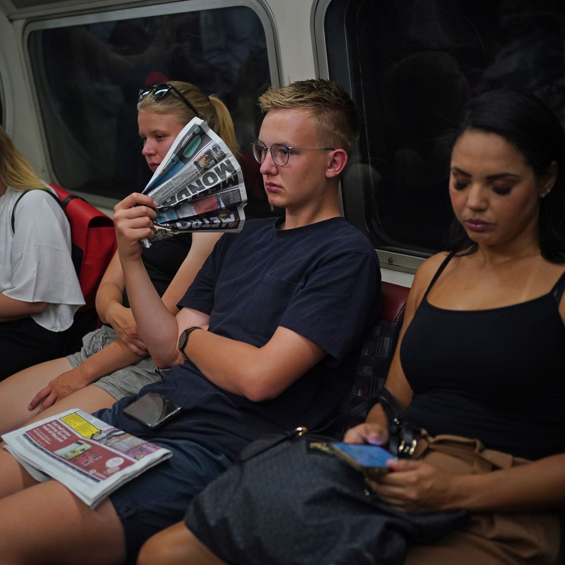 Man on London subway fans himself with newspaper during a heat wave.