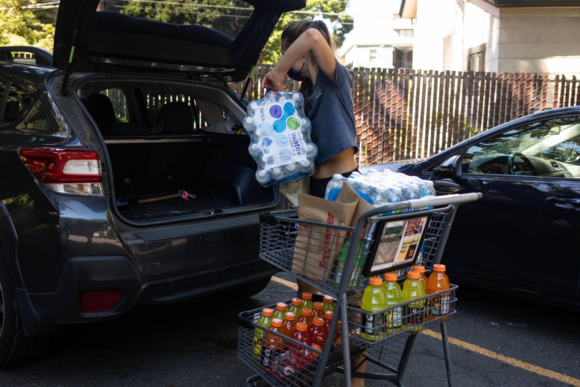 A shopper loads cases of water and Gatorade beverages into a car 