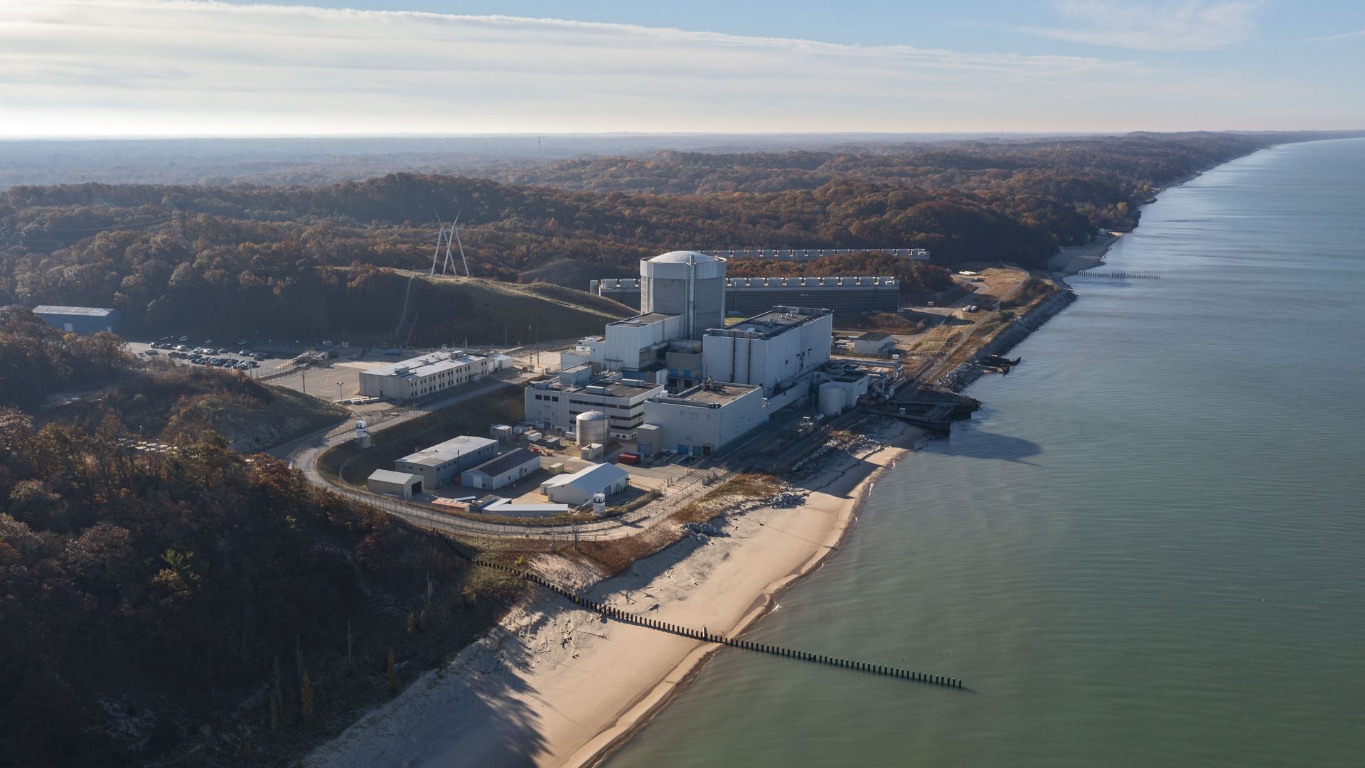 An aerial photo of Palisades Nuclear Plant in Michigan, on the shore of Lake Michigan, surrounded by woods with fall foliage.