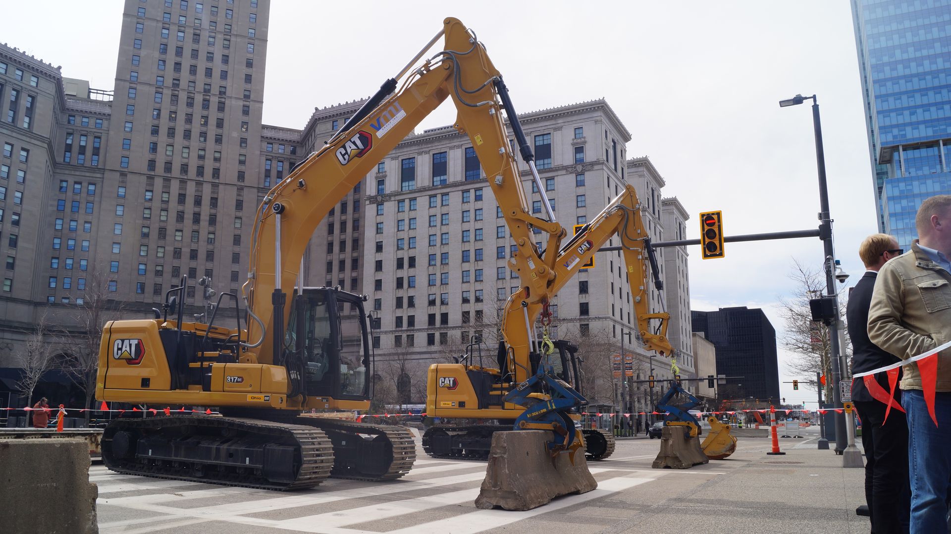 Two excavators on a street grip concrete jersey barriers. 