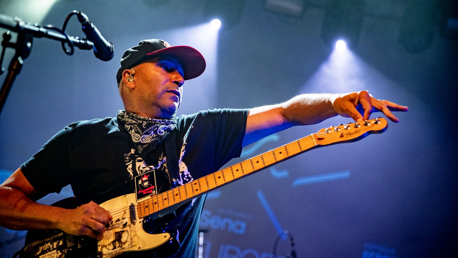 Photo of a man tuning a guitar on stage. 