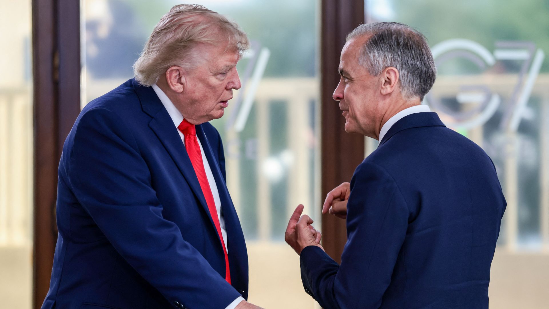 Trump — wearing a blue suit, a white collared shirt and a red tie — stands as he talks to Canada's Mark Carney, wearing a dark blue suit jacket and a collared shirt.