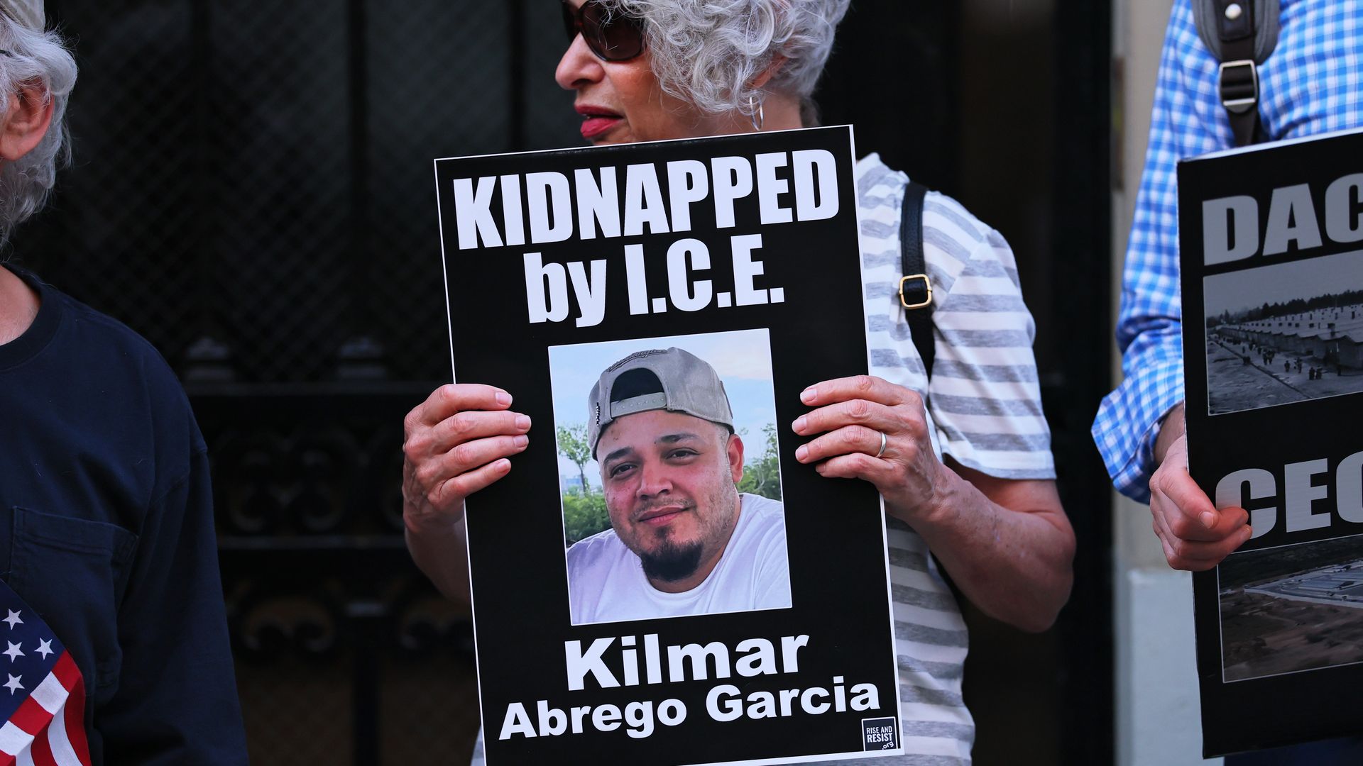 A protester holds a sign that says "KIDNAPPED BY I.C.E." and "Kilmar Abrego Garcia" with an image of a man deported to El Salvador.