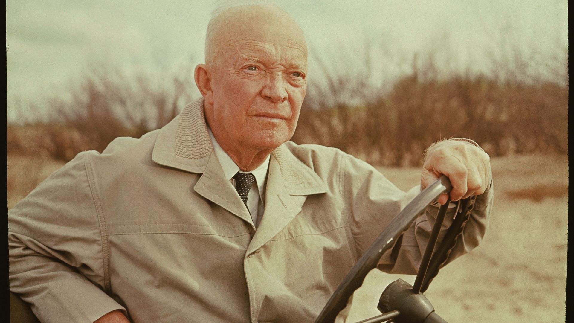 Former president Dwight D. Eisenhower sits in a cart with a jacket on while visiting old World War II sites. 