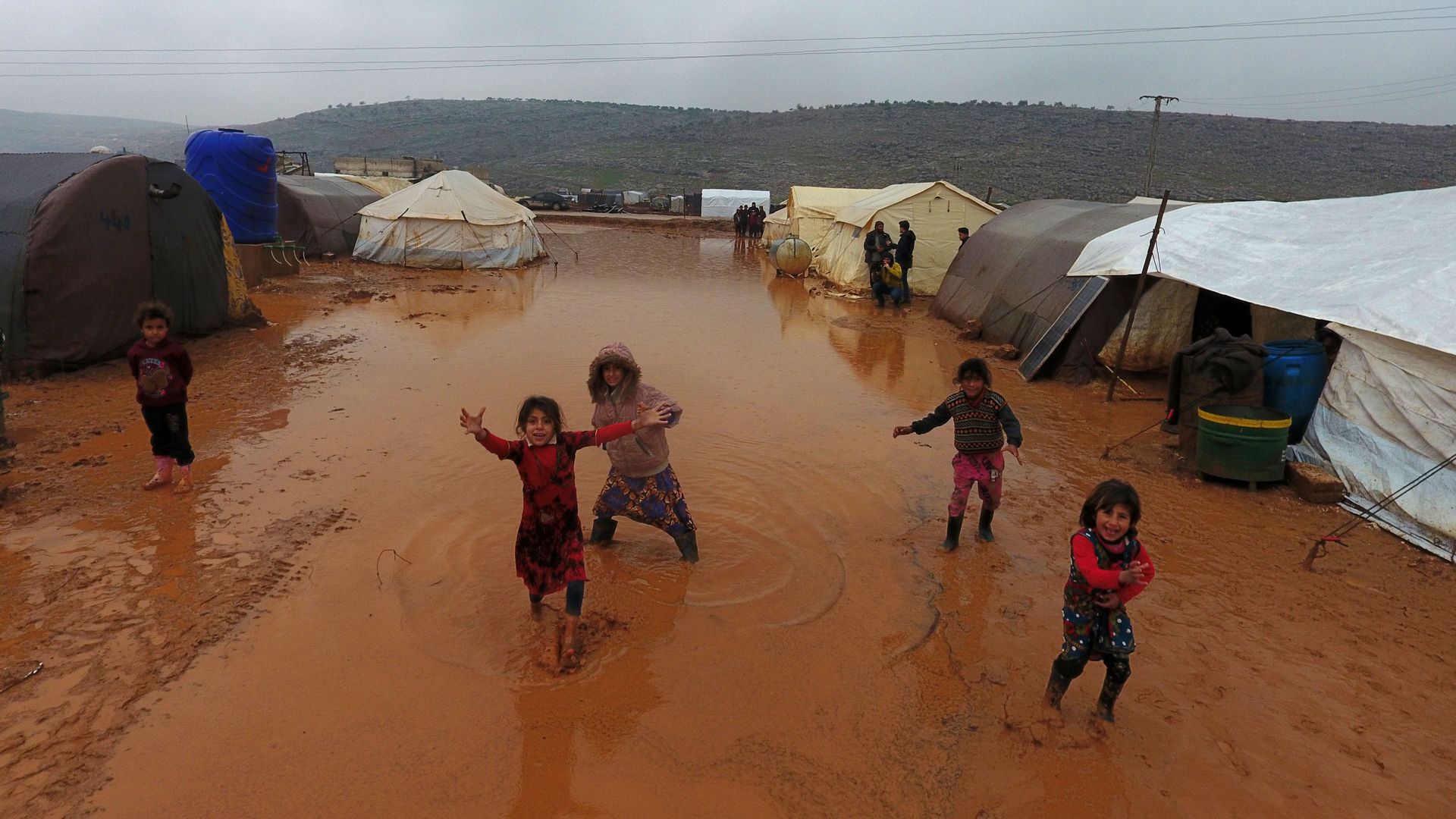 children playing in between tents on wet ground of refugee camp
