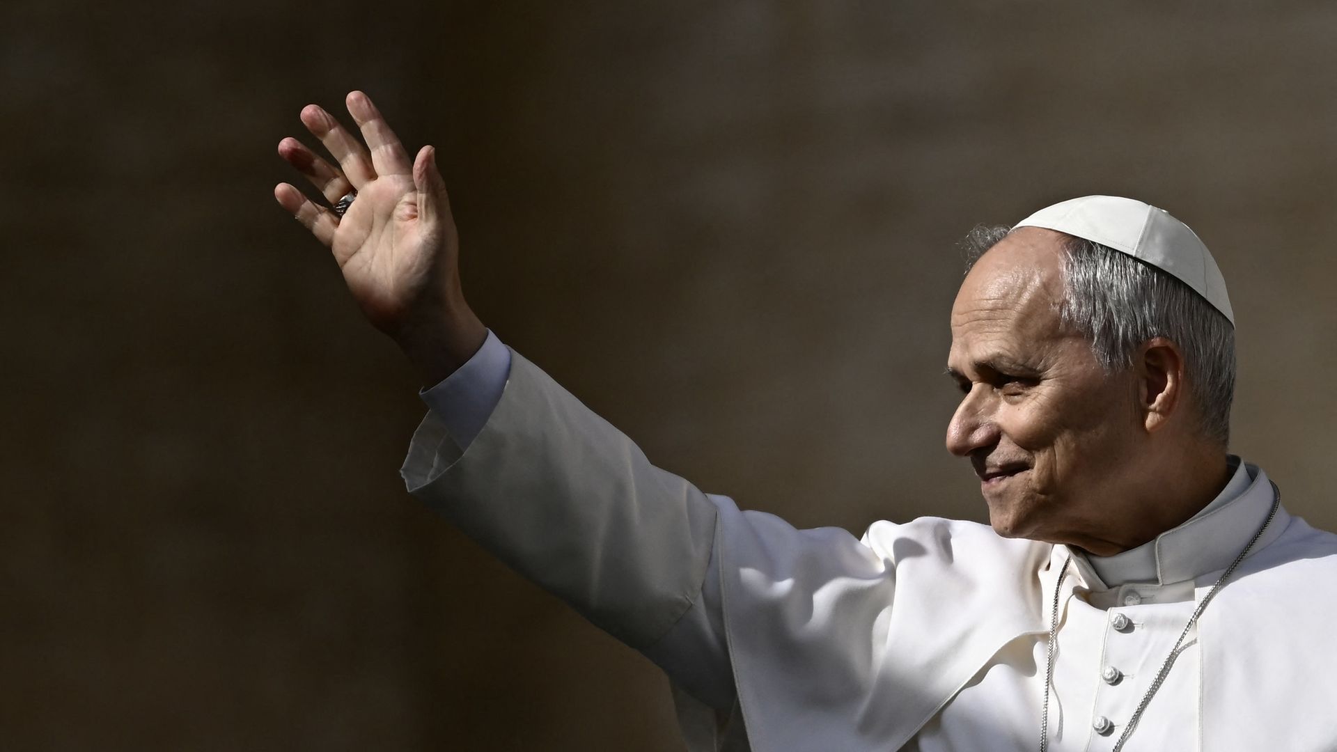 Pope Leo extends an arm to a Vatican crowd (not pictured) while wearing traditional white vestments.