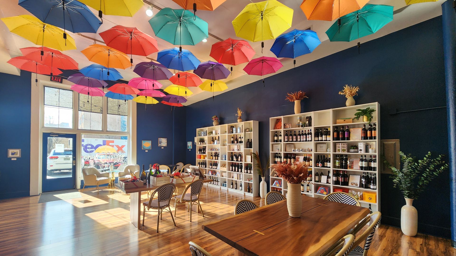 The dining room of an Italian sandwich shop with umbrellas on the ceiling, wine cases and tables.