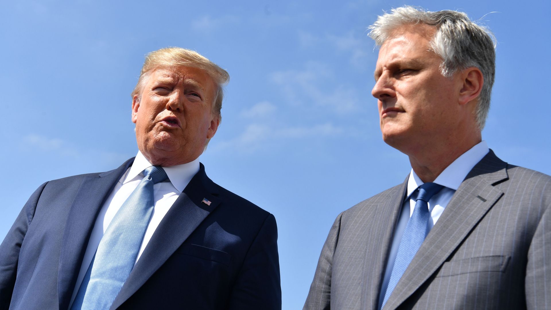 In this image, Trump and O'Brien speak to each other while both wearing suits. The blue sky is seen behind them.