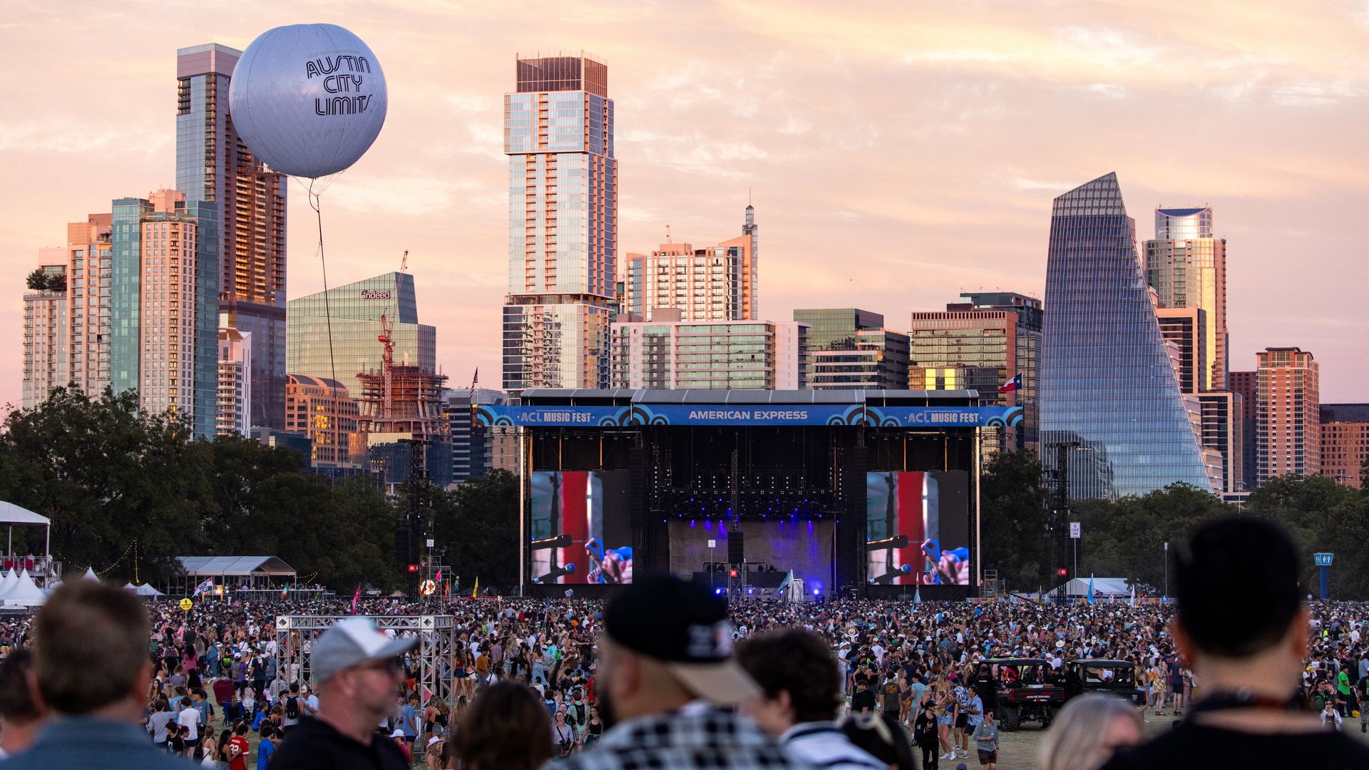 A photo of a crowd of people with the Austin skyline and a stage in the background.