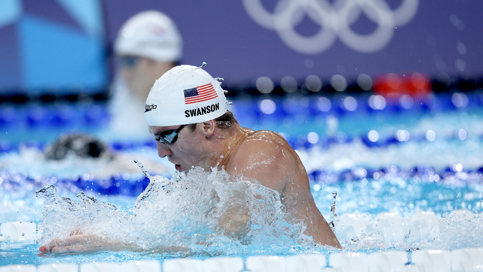 A swimmer with a white cap on with the USA flag and "Swanson" written under it.