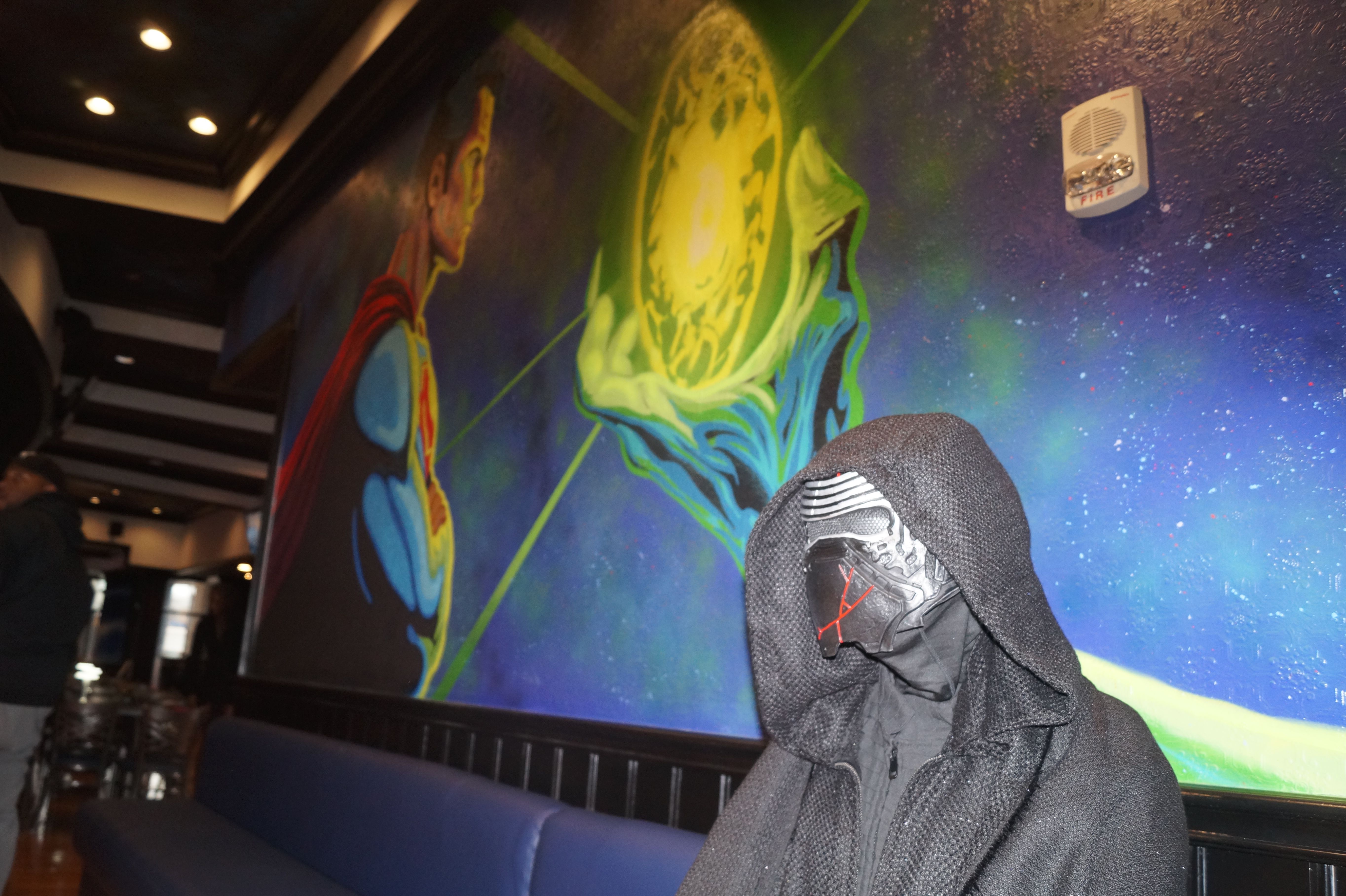 A Kylo Ren mannequin in front of a Superman mural. 