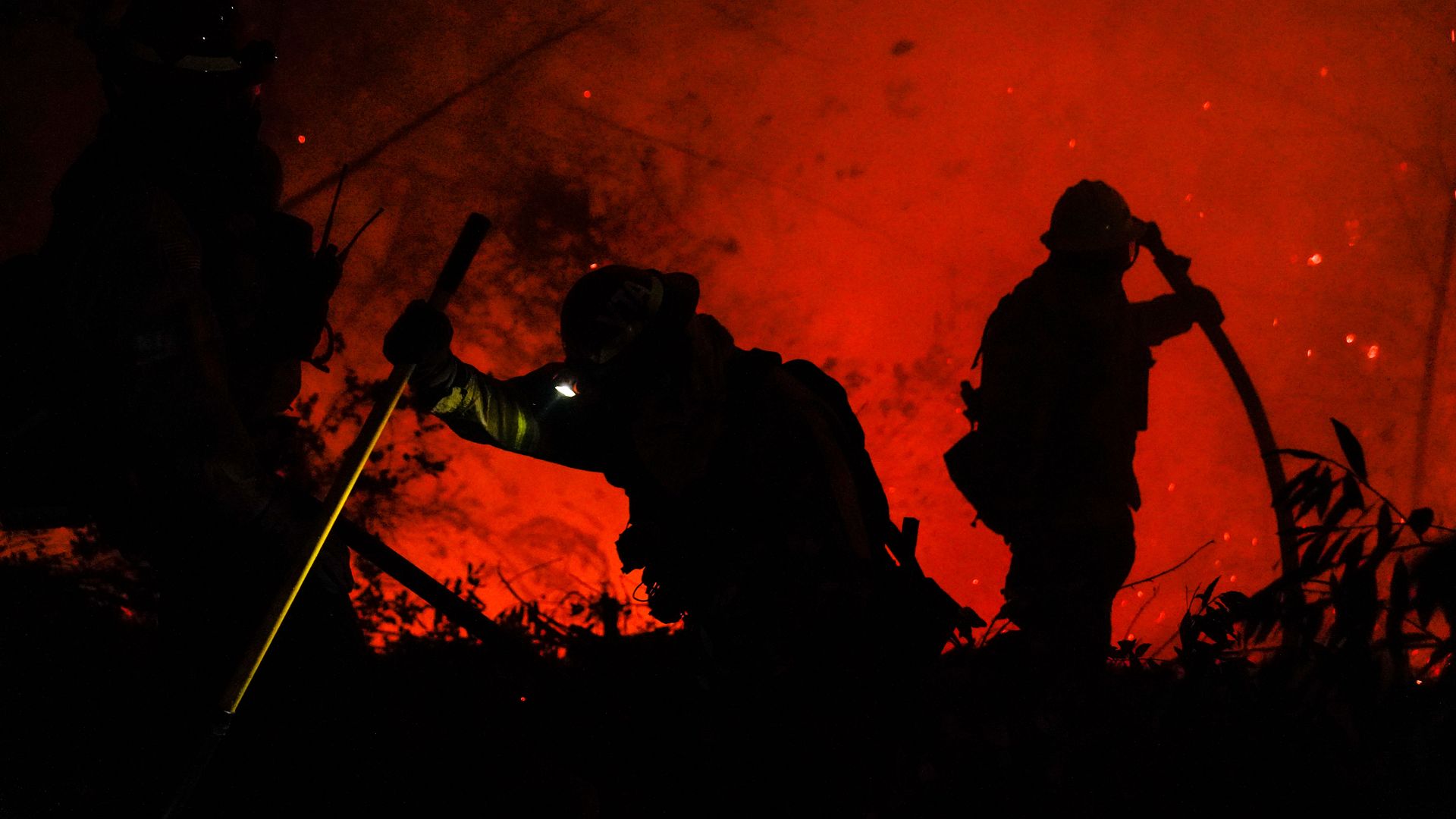 Photo of two firefighters' silhouettes against the backdrop of a roaring red fire