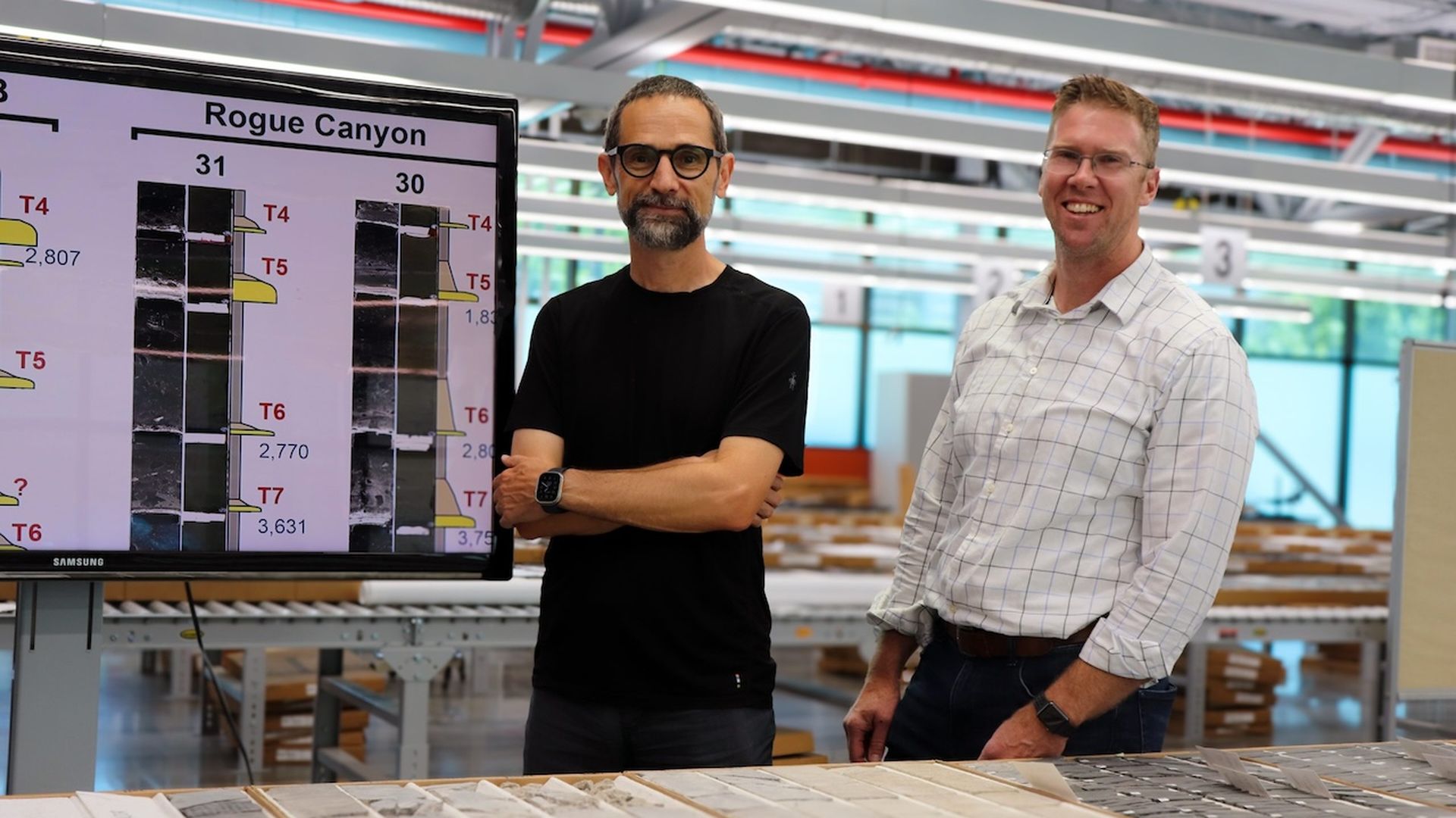 Two people pose for a photo in front of a screen that examines seafloor sediment.