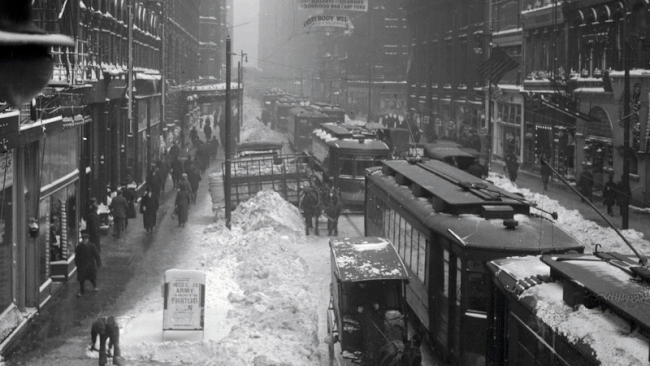 A GIF of two images taken over 100 years apart. One shows black and white horse and buggies and streetcars, while the other shows modern day traffic. 
