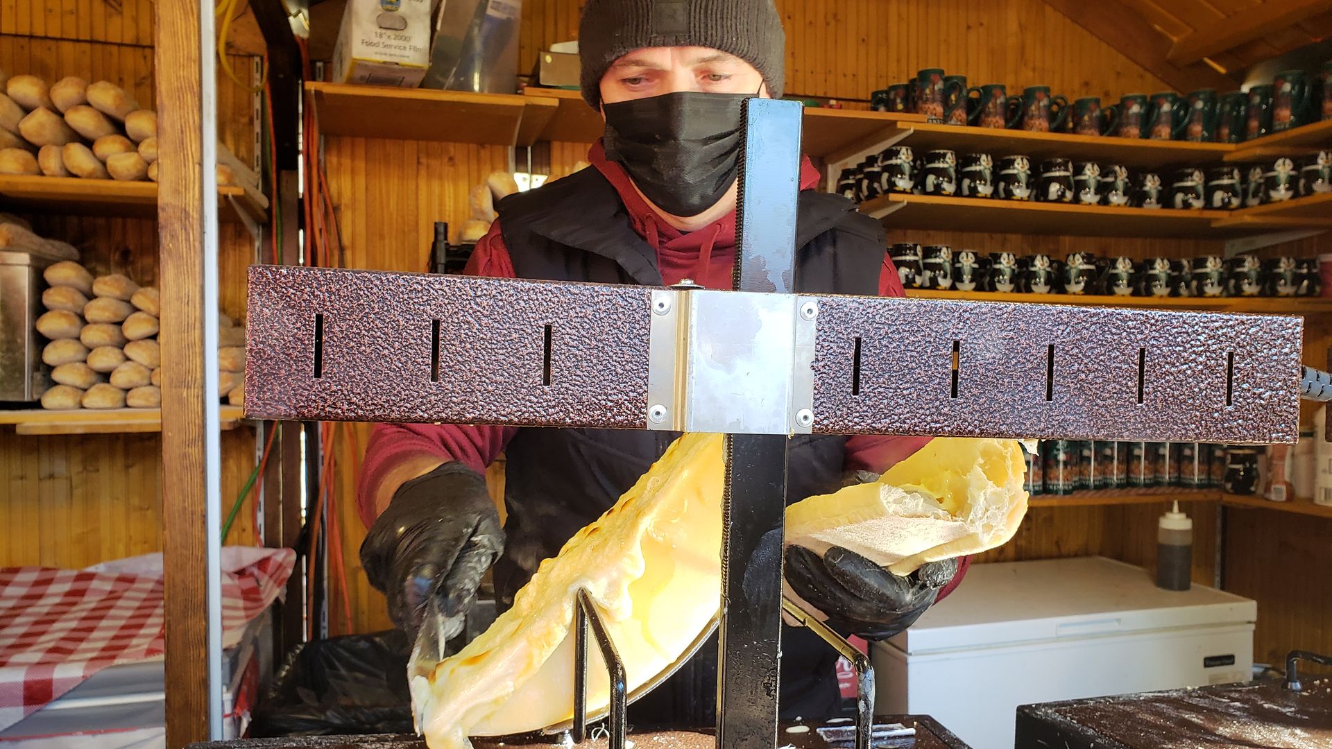 Woman scraping hot cheese from a cheese wheel. 